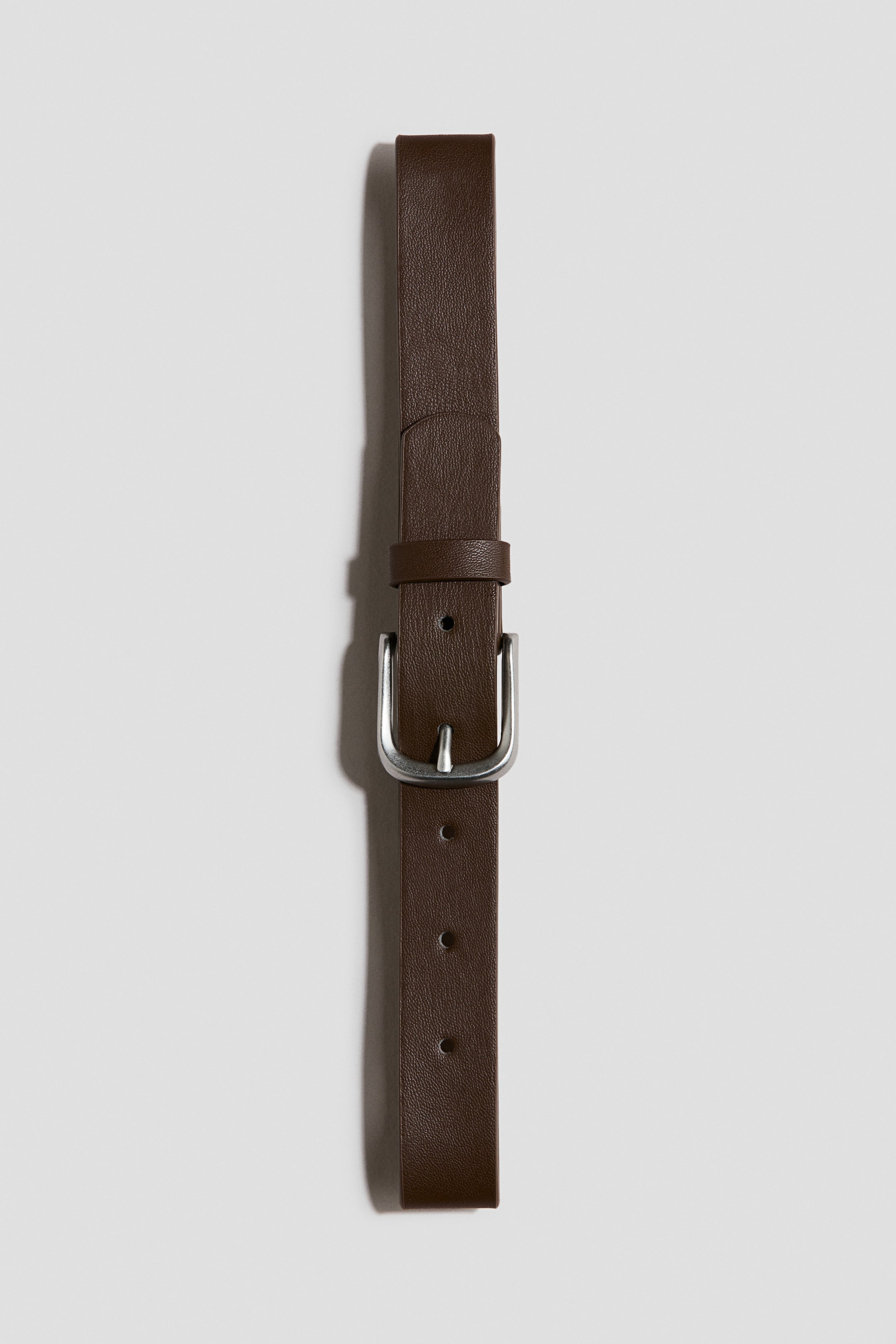 Voir une image plus grande: Une ceinture en cuir brun foncé est posée à plat et orientée verticalement. Elle présente une surface texturée, une boucle rectangulaire de ton argenté avec une seule broche, ainsi que plusieurs trous d'ajustement le long de sa longueur.
