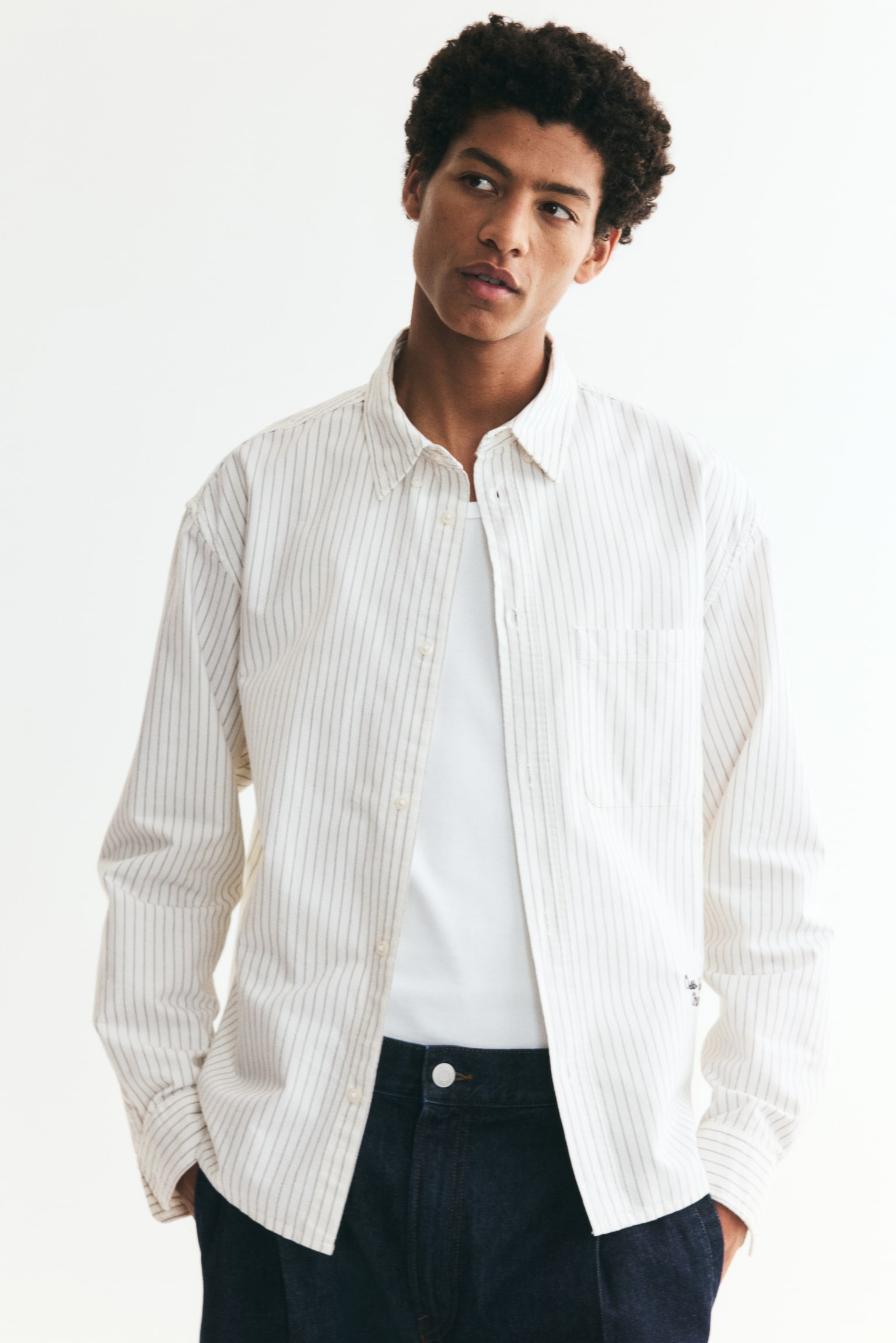 A long-sleeved shirt is showcased from the front, featuring a cream base with thin dark vertical stripes, a button-down collar, and a full button-front closure. It also includes a left chest patch pocket, buttoned cuffs, and black embroidered text reading "Cross-Country Champs" on the right chest. - 1