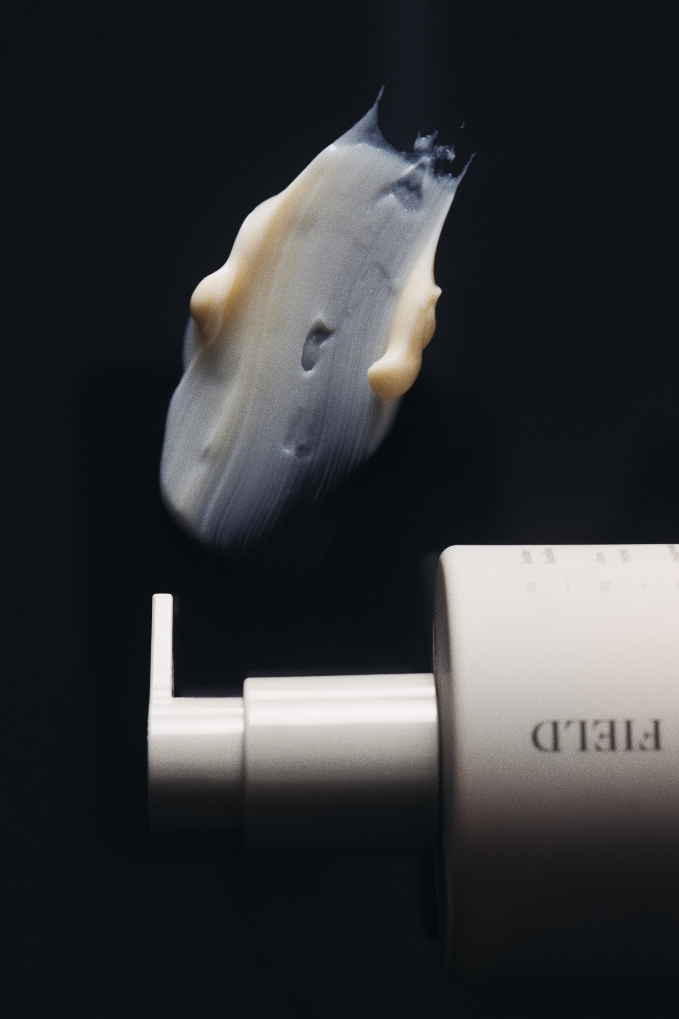 View larger image: A cream-colored hand lotion bottle with a smooth matte finish is lying horizontally, showcasing its pump dispenser and minimalist branding, with a thick, textured smear of off-white cream appearing above the pump.
