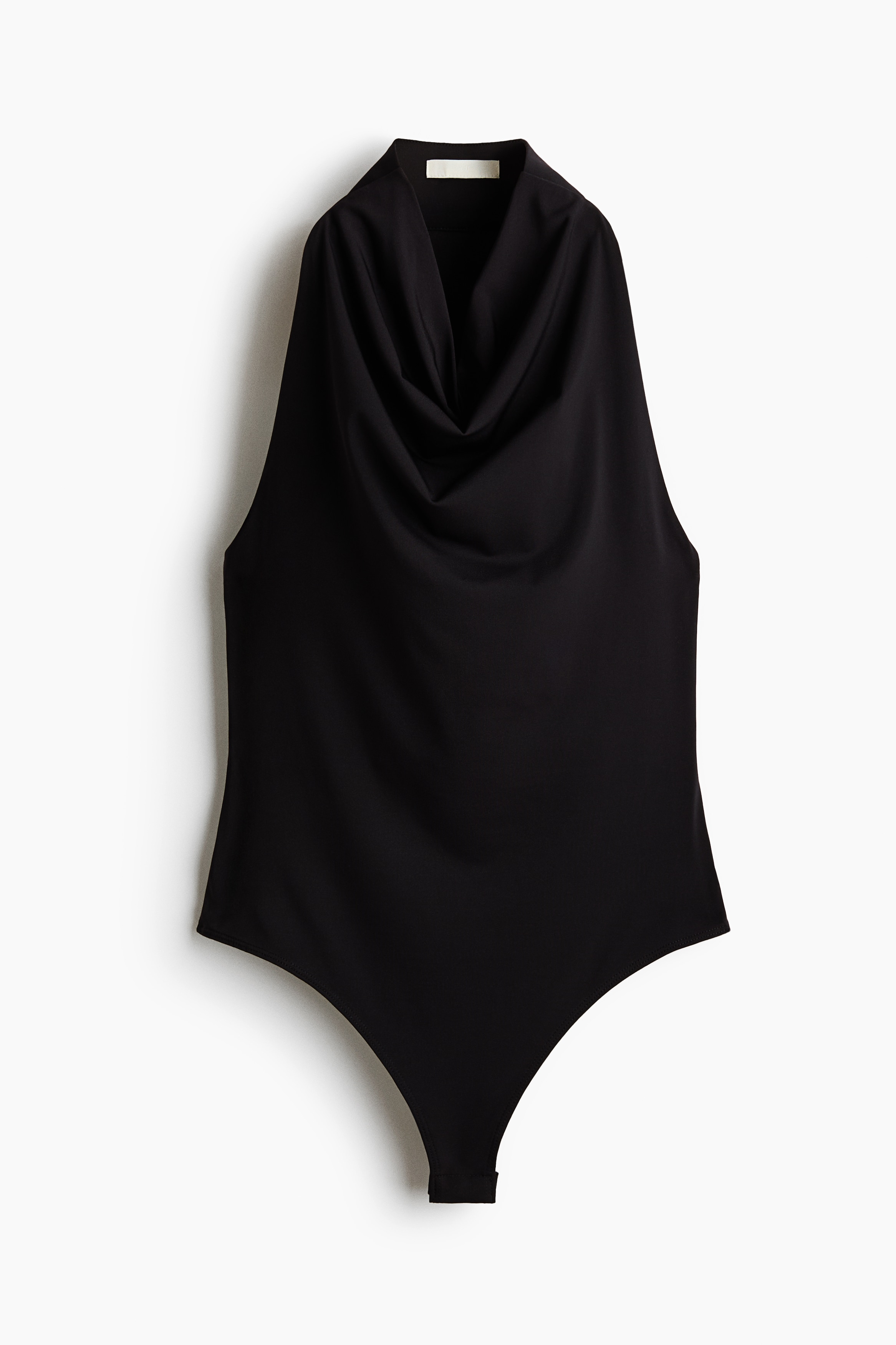 A sleeveless, dark-coloured bodysuit featuring a draped cowl neck and a narrow cut at the shoulders is being worn by the model. The fitted bodysuit is styled tucked into a pair of wide-leg trousers.