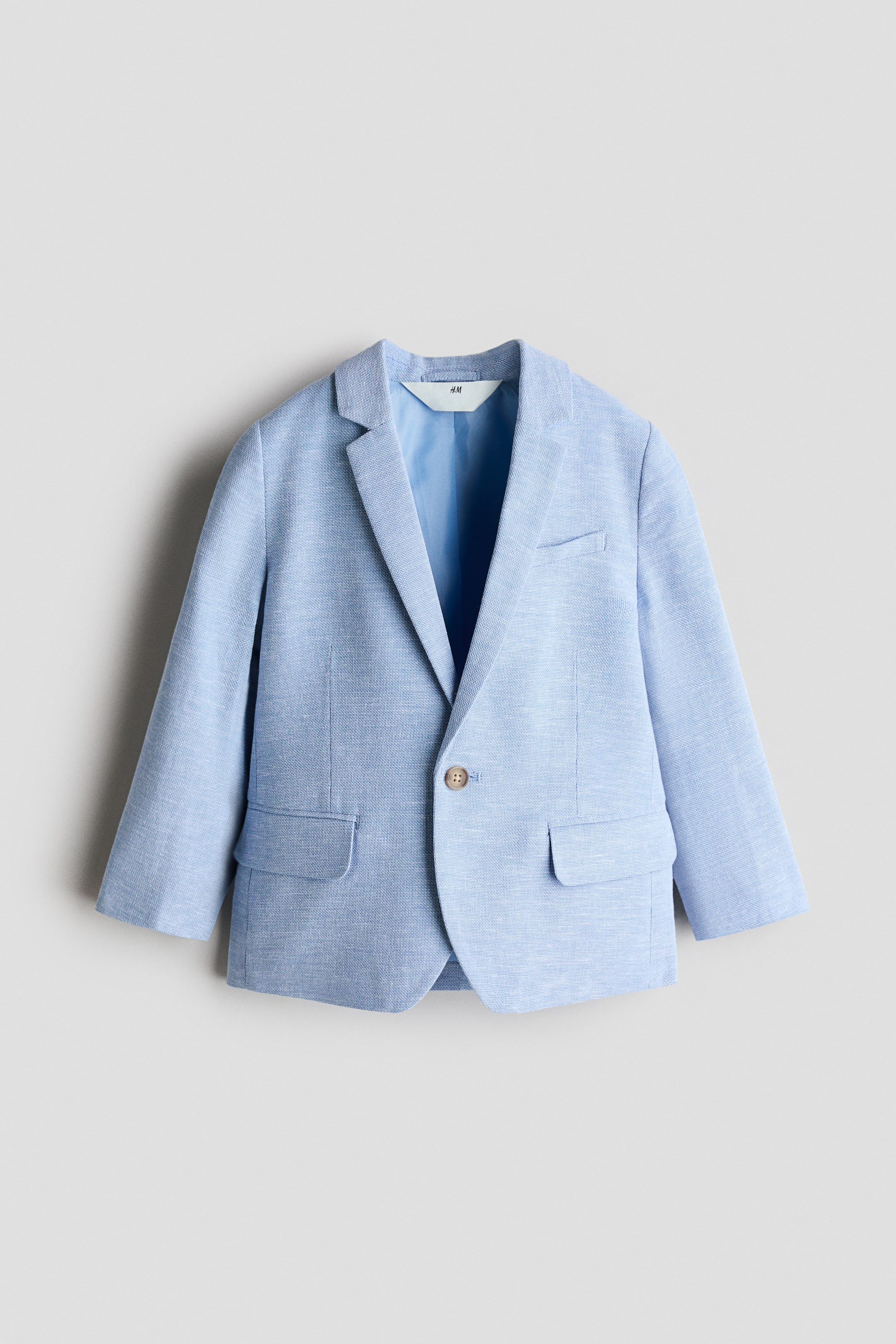 View larger image: The jacket, displayed from the front, is crafted from a light blue woven cotton and linen blend fabric. It features notch lapels, a single-button closure, a faux chest pocket, and two faux flap pockets.