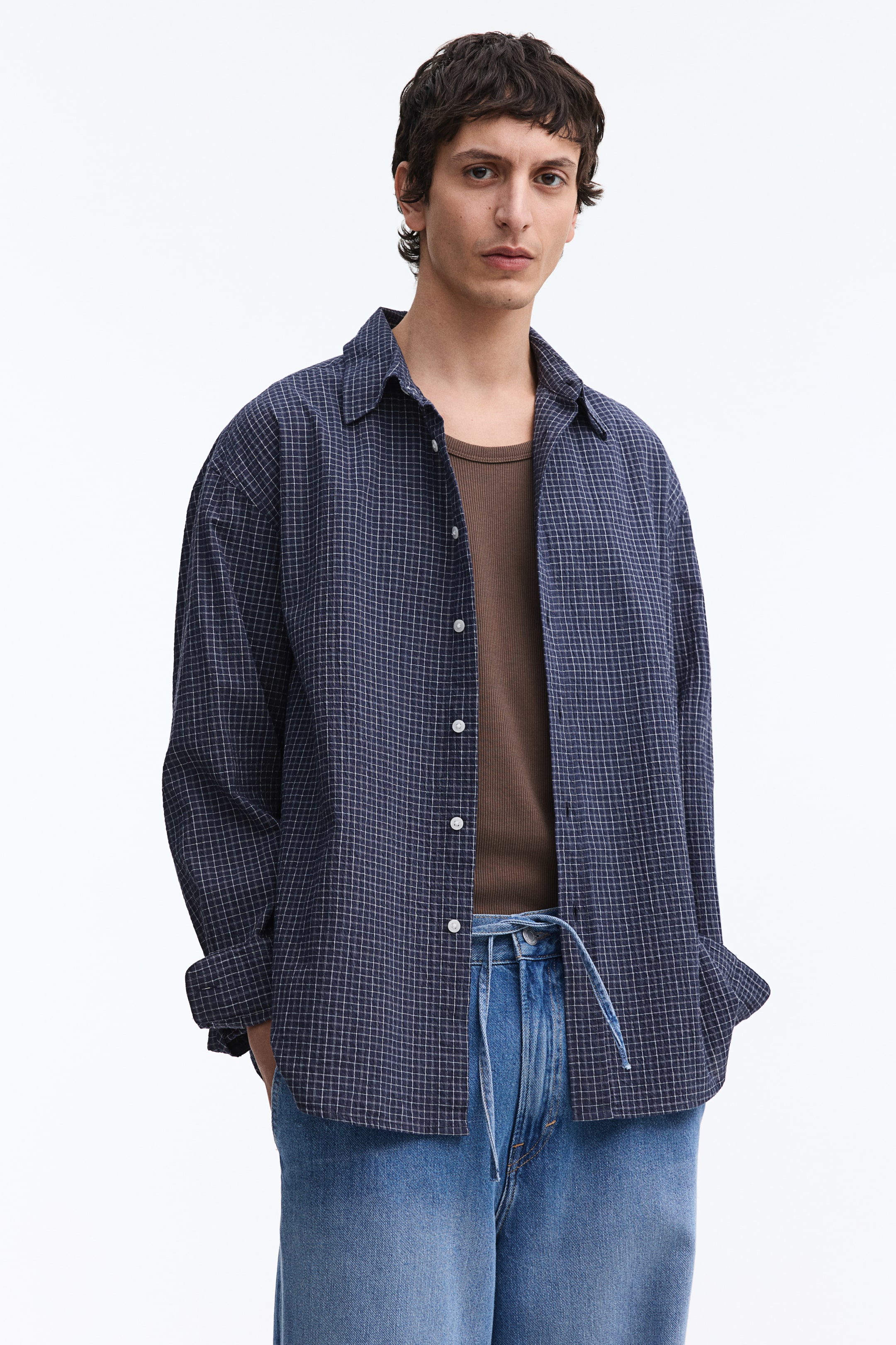 View larger image: A navy blue plaid shirt is showcased, highlighting a white grid pattern and white front buttons. It is styled open over a brown ribbed tank top, with its long sleeves rolled up at the cuffs.