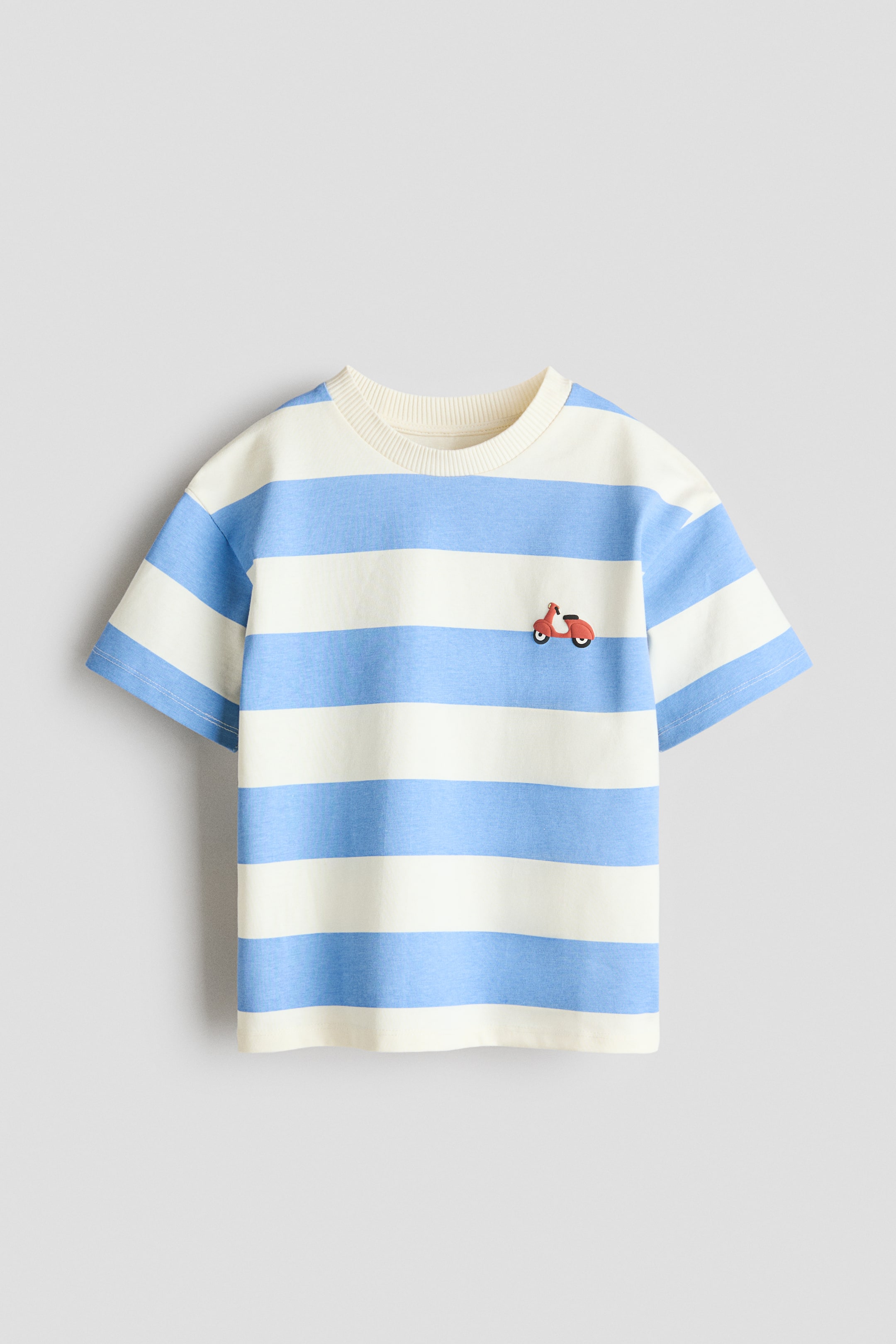 拡大画像を表示: ルーズフィットTシャツは、フロントを見せており、ライトブルーとオフホワイトの横縞模様が特徴です。ラウンドリブトリムのネックライン、ドロップショルダー、左胸には小さな赤いスクーターの刺繍が施されています。