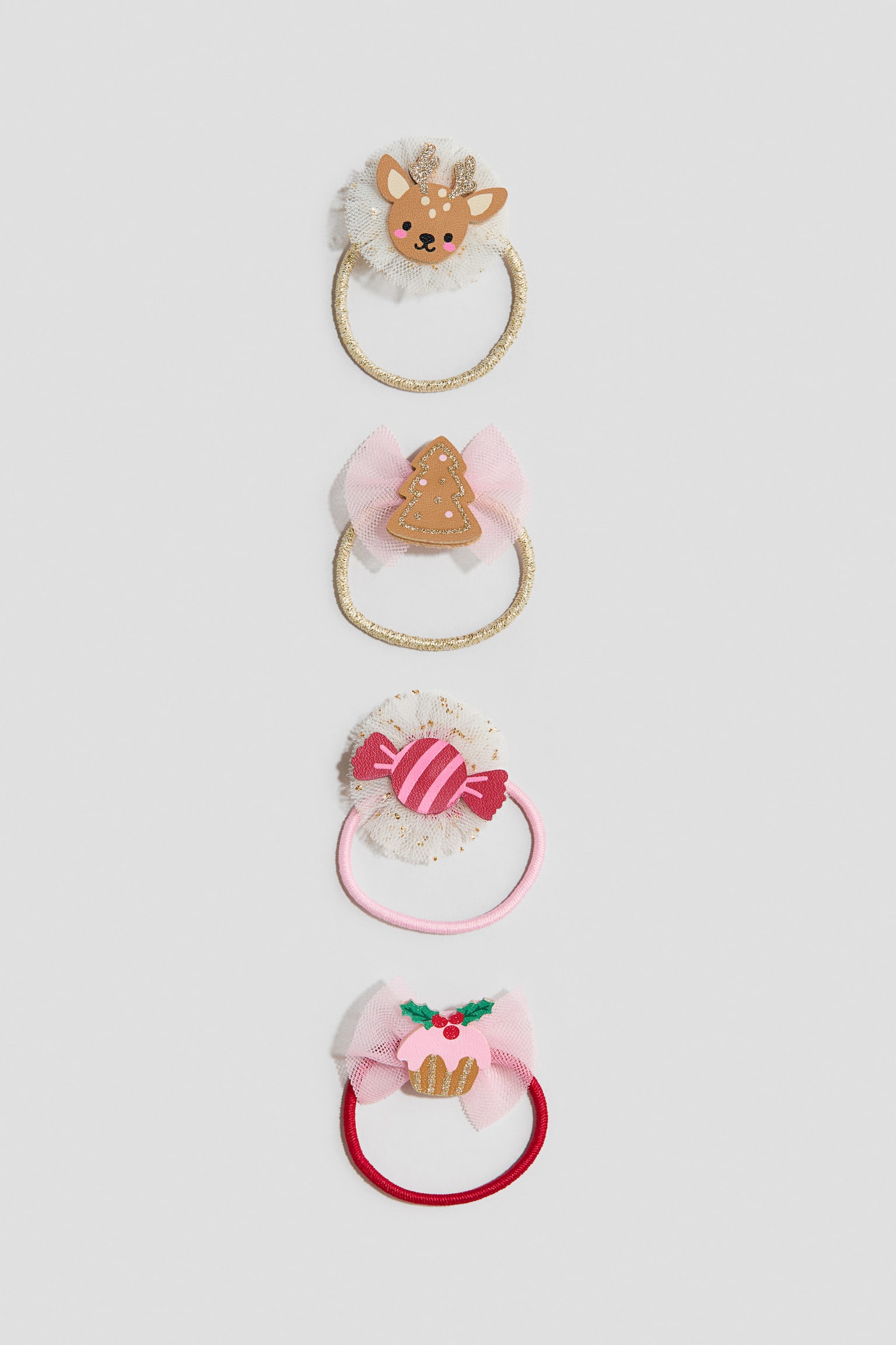 Quatre chouchous festifs sont prÃ©sentÃ©s en ligne verticale, vus de face, chacun avec un Ã©lÃ©ment dÃ©coratif de NoÃ«l unique. Les modÃ¨les comprennent une tÃªte de renne avec des bois scintillants sur un bandeau dorÃ©, un sapin en pain dâÃ©pices sur un nÅud en tulle rose avec un bandeau dorÃ©, un bonbon emballÃ© rose sur un pompon en tulle blanc mouchetÃ© avec un bandeau rose, et un cupcake de NoÃ«l ornÃ© de houx sur un nÅud en tulle rose avec un bandeau rouge.