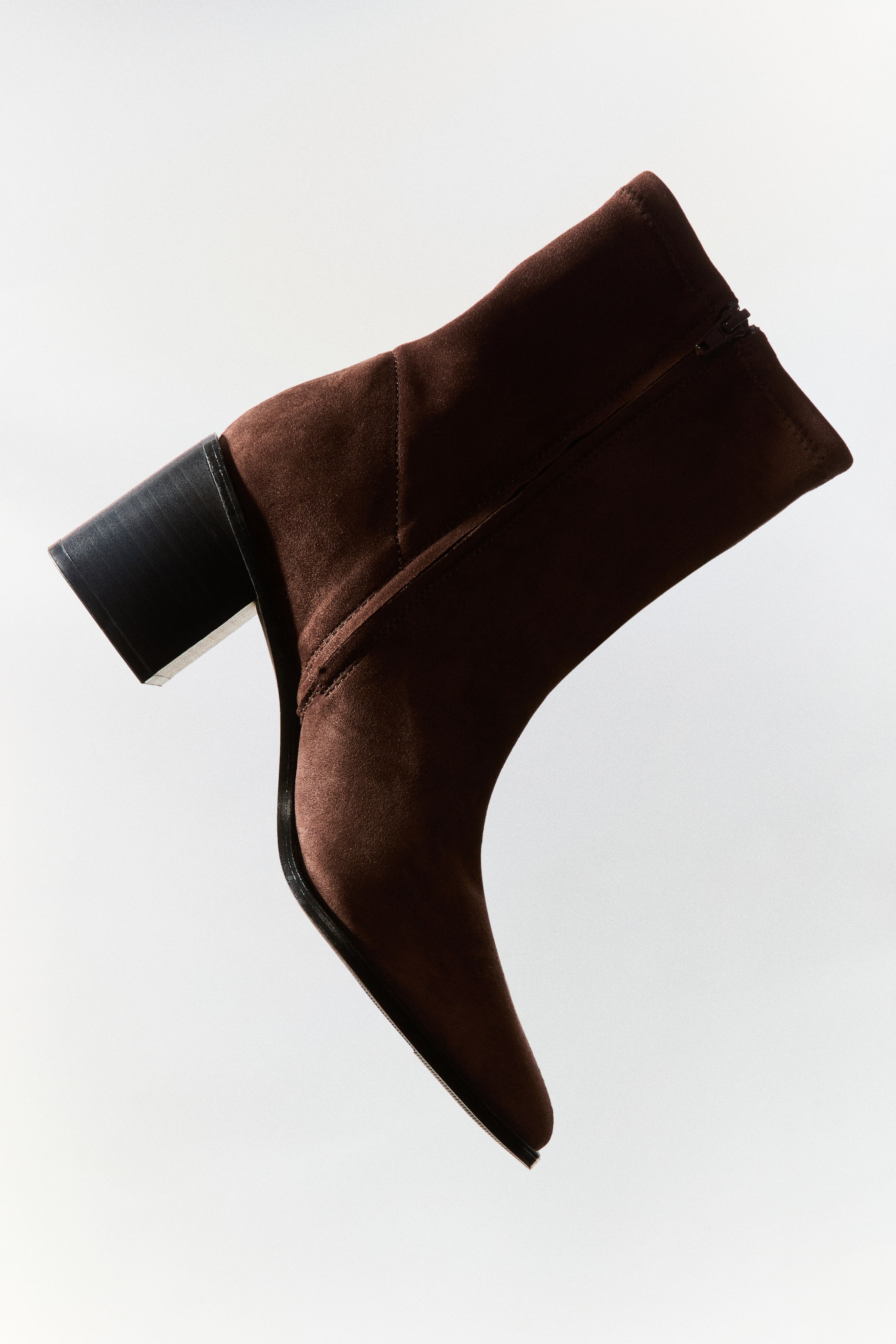 View larger image: A dark brown suede-textured ankle boot is shown in side profile, featuring a chisel toe, a black block heel, and a side zip closure along the fitted shaft.