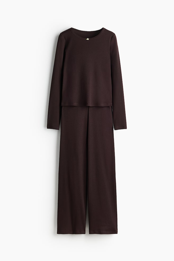 Ribbed jersey pyjamas are featuring a dark brown, long-sleeved top and matching long trousers, presented from the front. The top is showing a round neckline with a scalloped trim and a small, light-colored button detail, while the trousers are designed with straight legs and front pleats. - 1