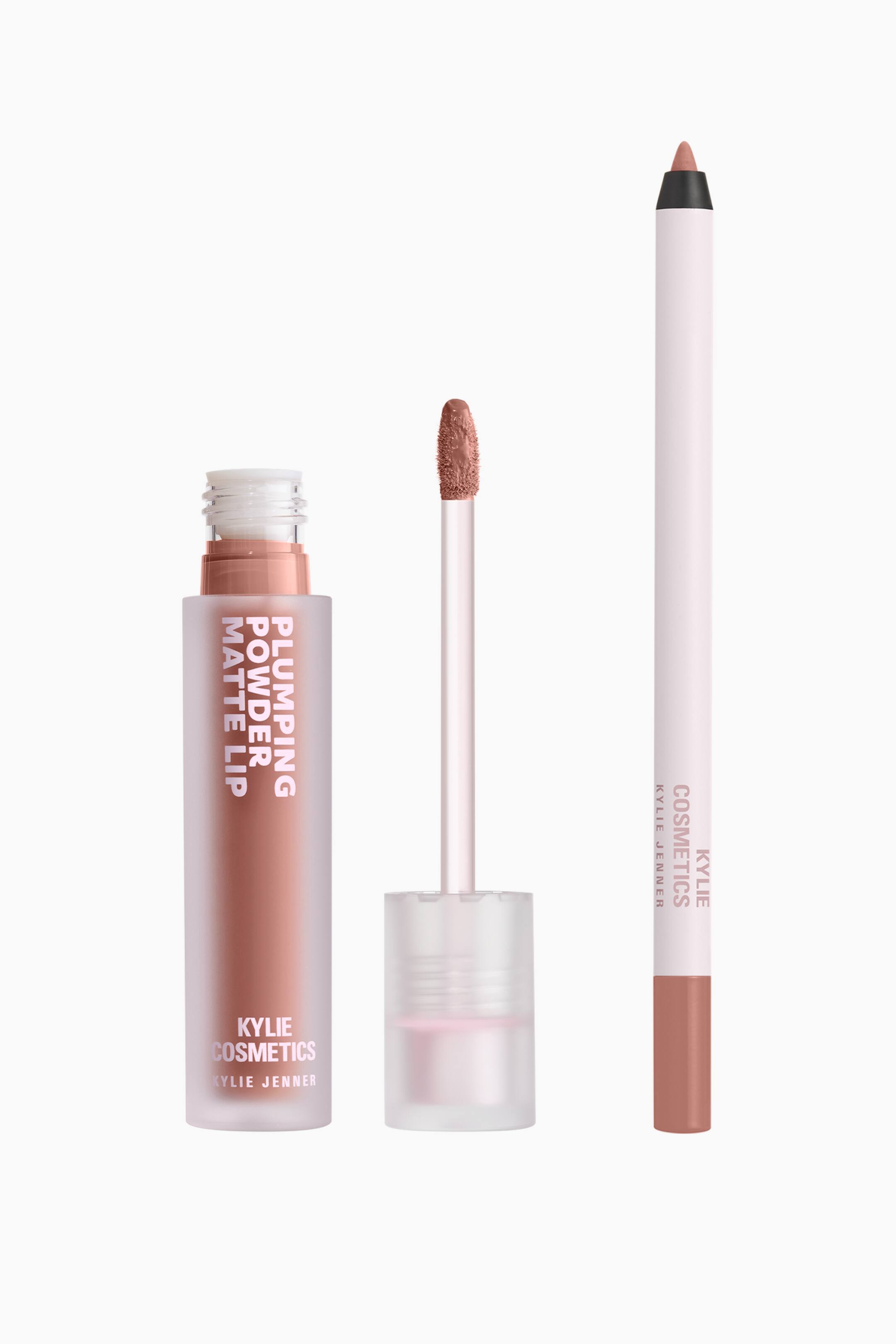Visa större bild: Kylie Cosmetics Plumping Matte Lip Kit står upprätt och visar upp sina delar i en varm nude-rosa nyans. En öppen frostad tub med flytande läppstift visar produktens färg tillsammans med sin upprättstående applikatorstav, medan en matchande smal läppenna står till höger.