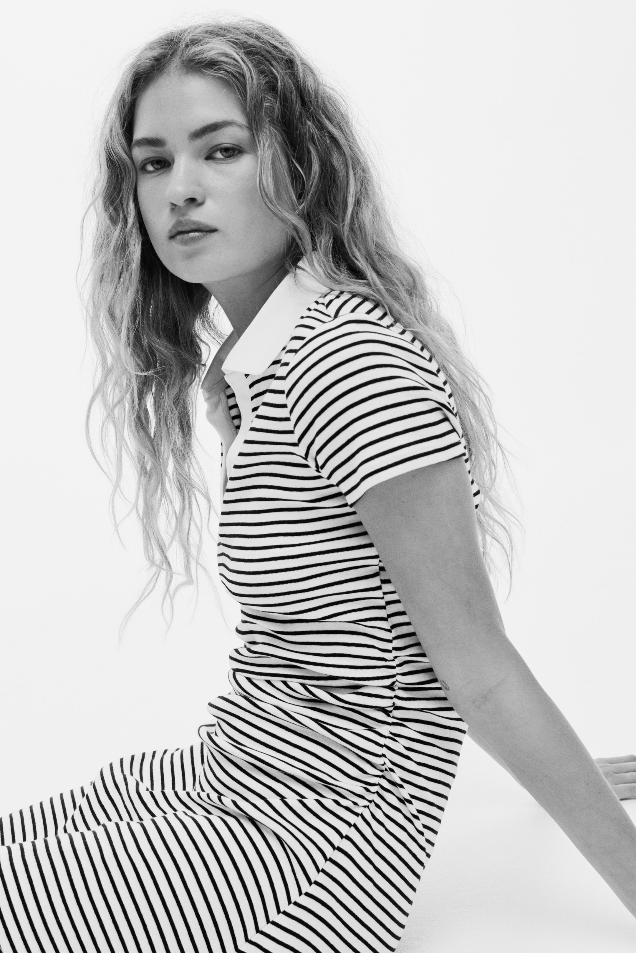 View larger image: The striped polo dress features horizontal black and white stripes, a white polo collar, and short sleeves. It is ruched along one side, creating vertical folds down its length.