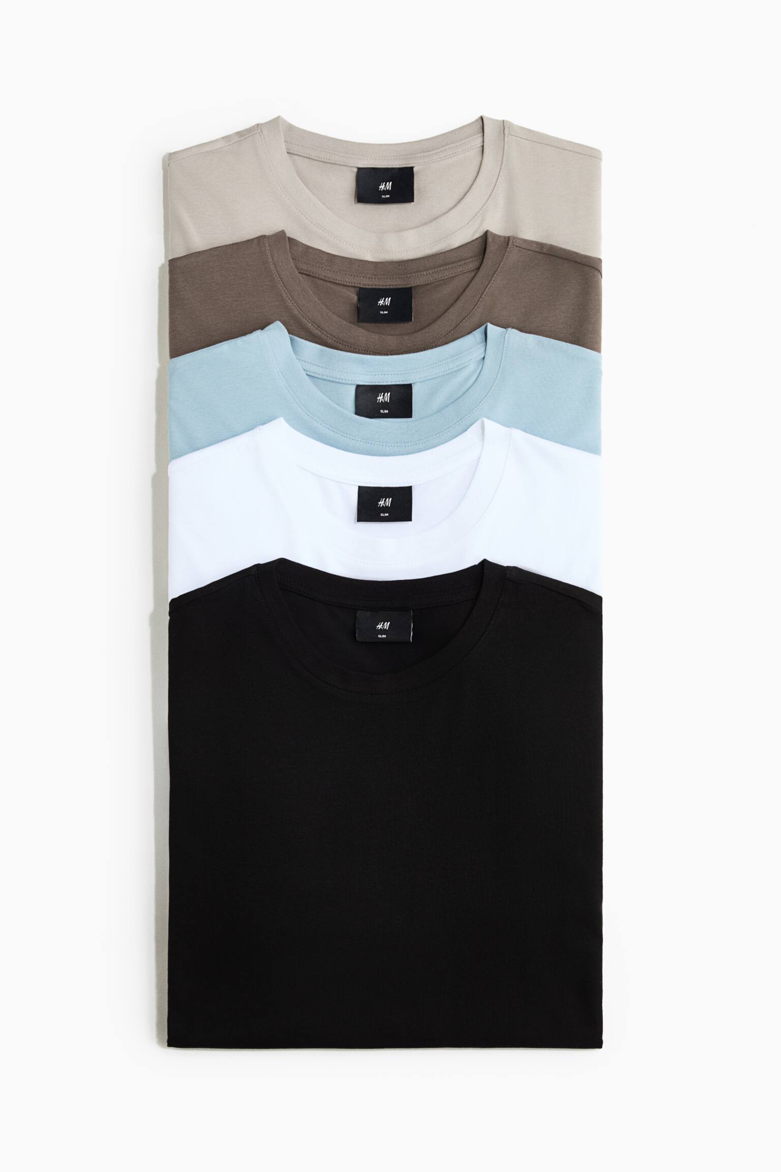 A stack of five slim-fit cotton jersey T-shirts is shown from the front, featuring round, rib-trimmed necklines. The folded T-shirts display a colour palette of light beige, brown, light blue, white, and black.