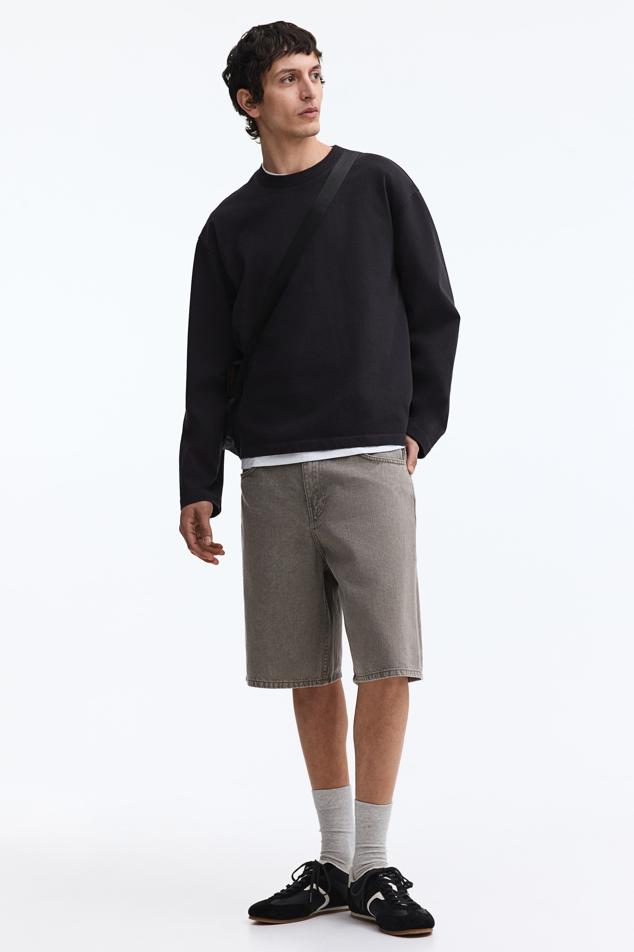 View larger image: A black crewneck sweatshirt is showcased, angled slightly to the right. It boasts a relaxed fit with long sleeves, ribbed cuffs, and a ribbed hem. A white t-shirt is layered underneath, with its hem visibly extending below the sweatshirt.