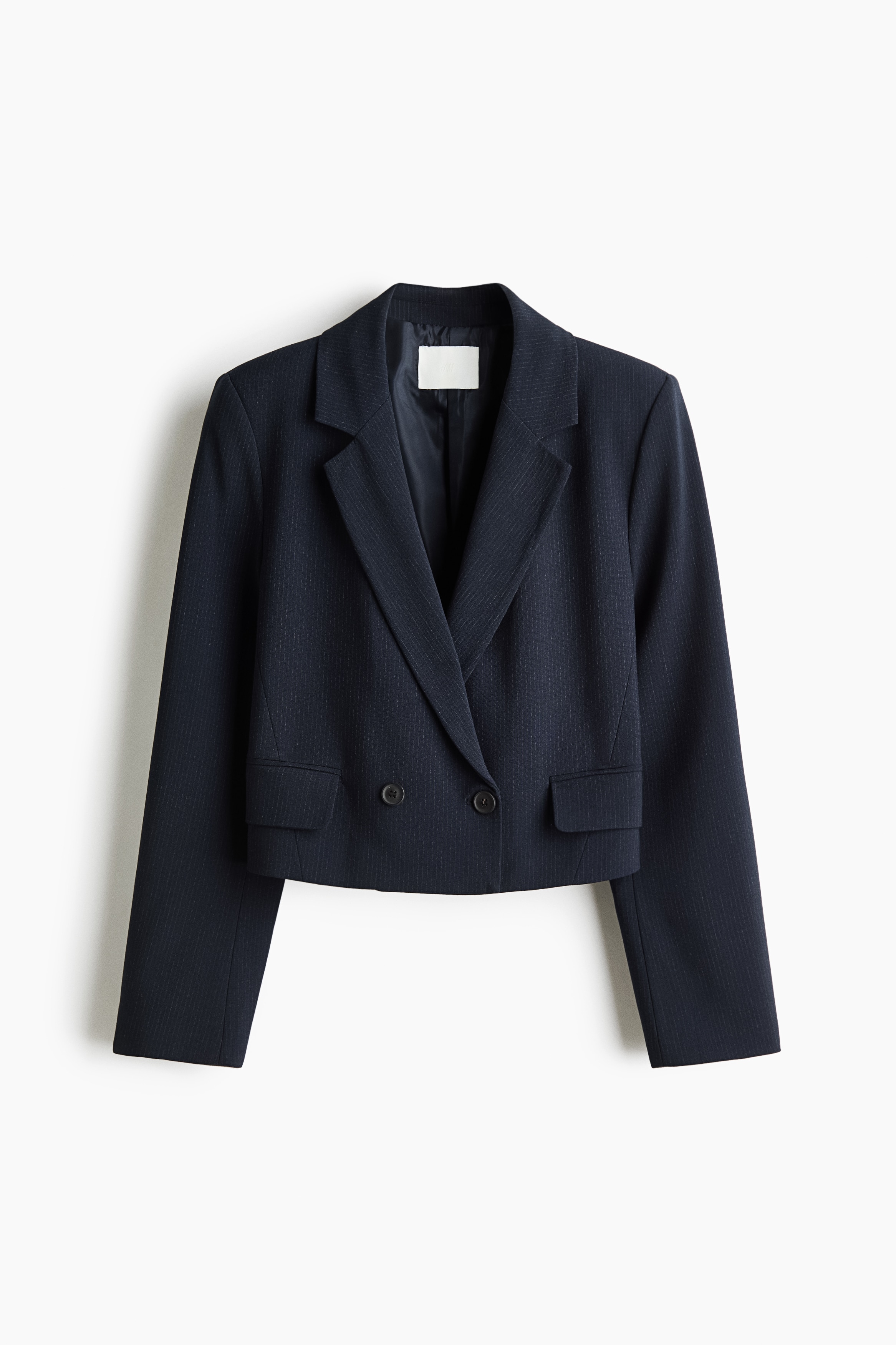 Ein kurz geschnittener, zweireihiger marineblauer Blazer wird vom Model getragen, kombiniert mit einem weiÃen Hemd mit Kragen und einem leuchtend blauen Halstuch. Der Blazer verfügt über fallende Revers und Frontknöpfe und wird mit hellblauen Jeans kombiniert.