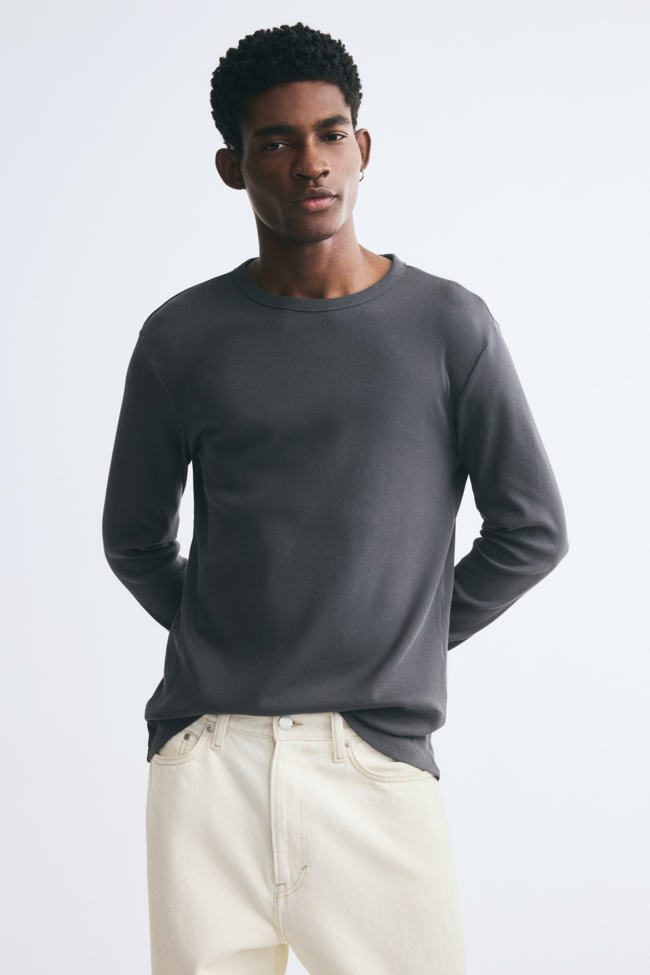 View larger image: The model is wearing a dark grey ribbed cotton jersey long-sleeve T-shirt, featuring a crew neckline and a slim fit. The tee is styled with a pair of off-white jeans.