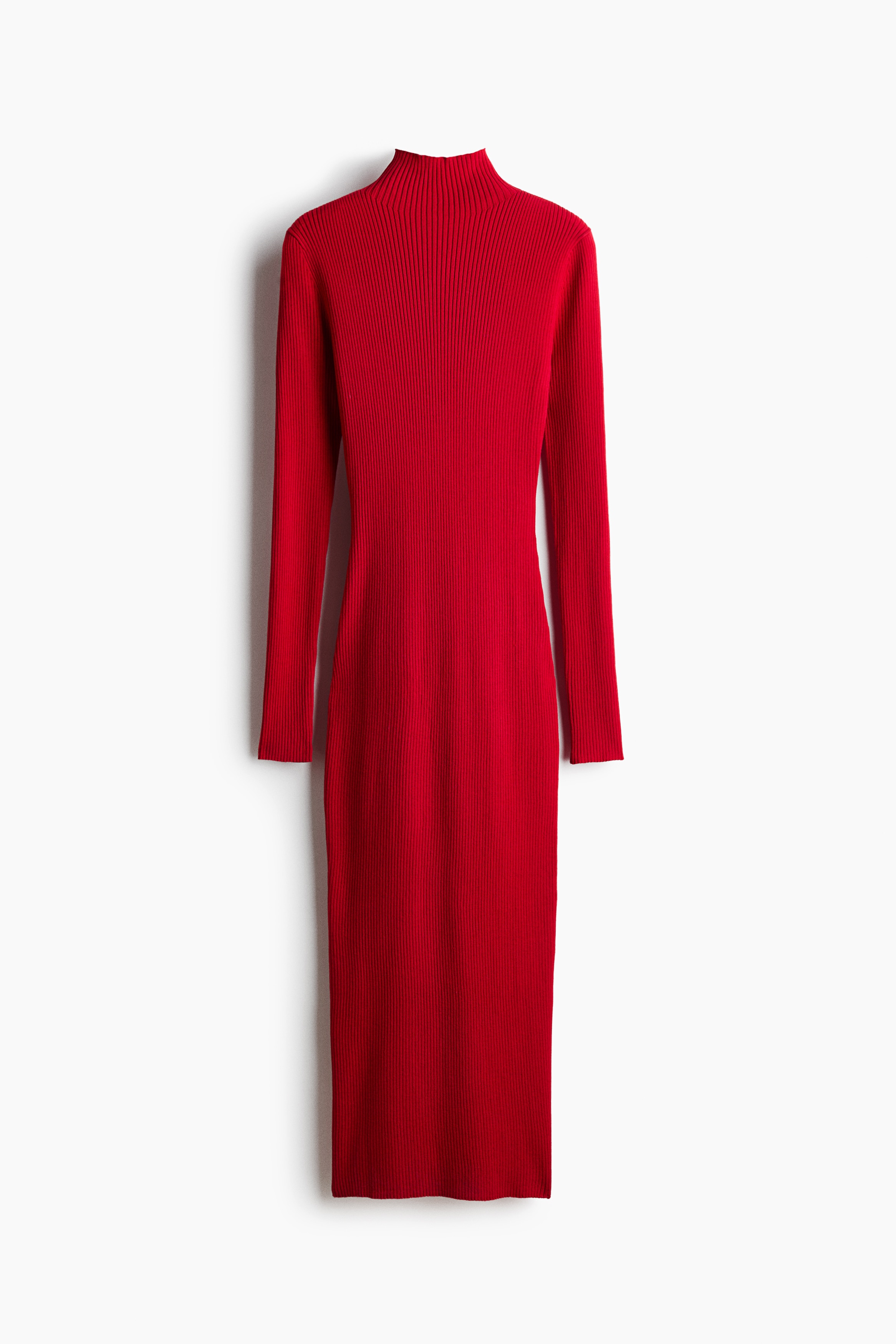The model is wearing a long, fitted red dress in a soft rib knit, featuring a high neck and long sleeves. A matching red cardigan is tied around the waist, and the dress is styled with high-heeled black leather boots.