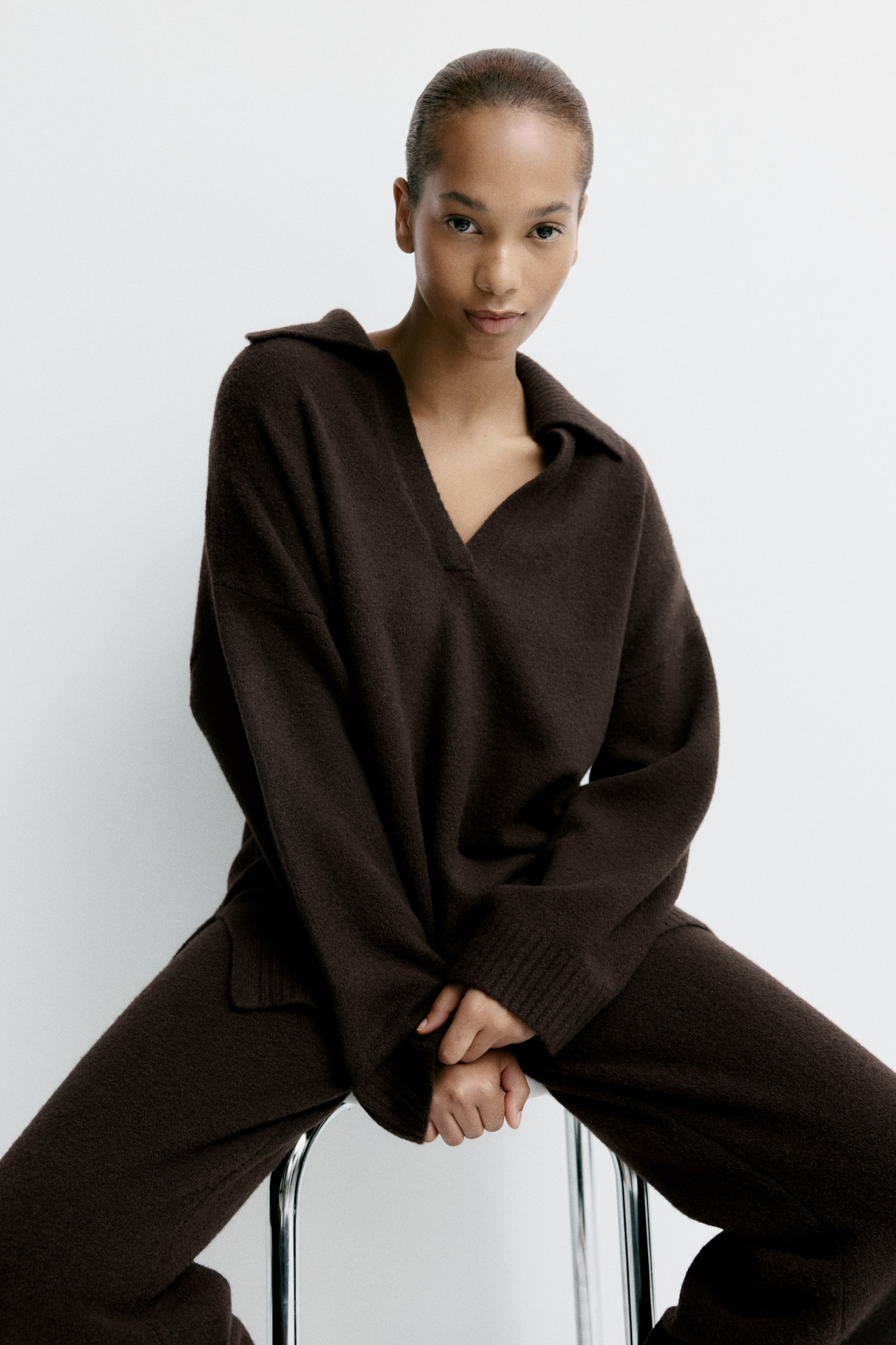 View larger image: A dark-brown knit set features a long-sleeved sweater with a spread collar and V-neck opening, and matching relaxed-fit pants. The sweater has ribbed cuffs on the sleeves and a relaxed hem.