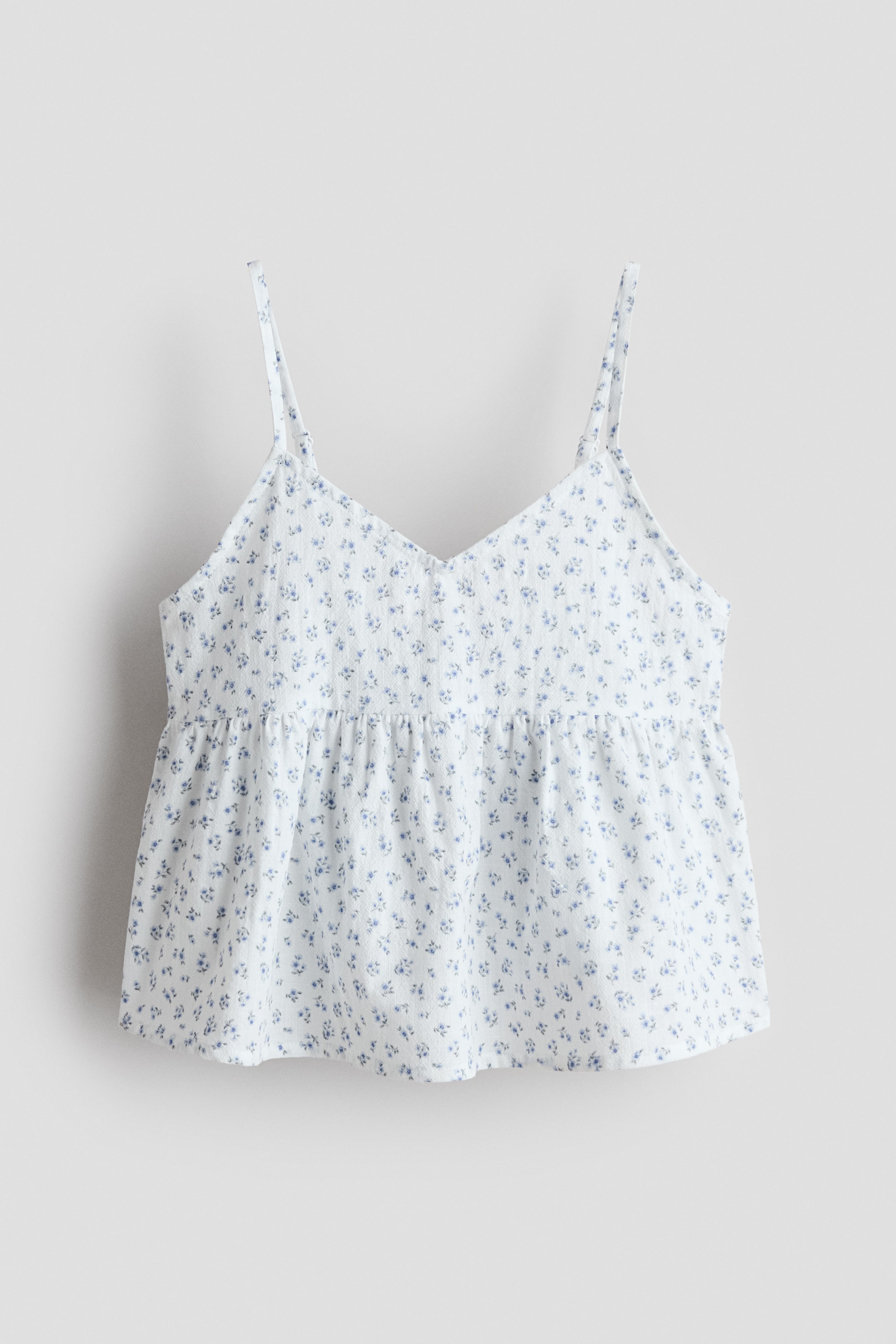 View larger image: A white top in a cotton weave with a blue floral print is displayed from the FRONT. It features a V-shaped neckline, narrow shoulder straps, a gathered seam at the waist, and a gently flared peplum.