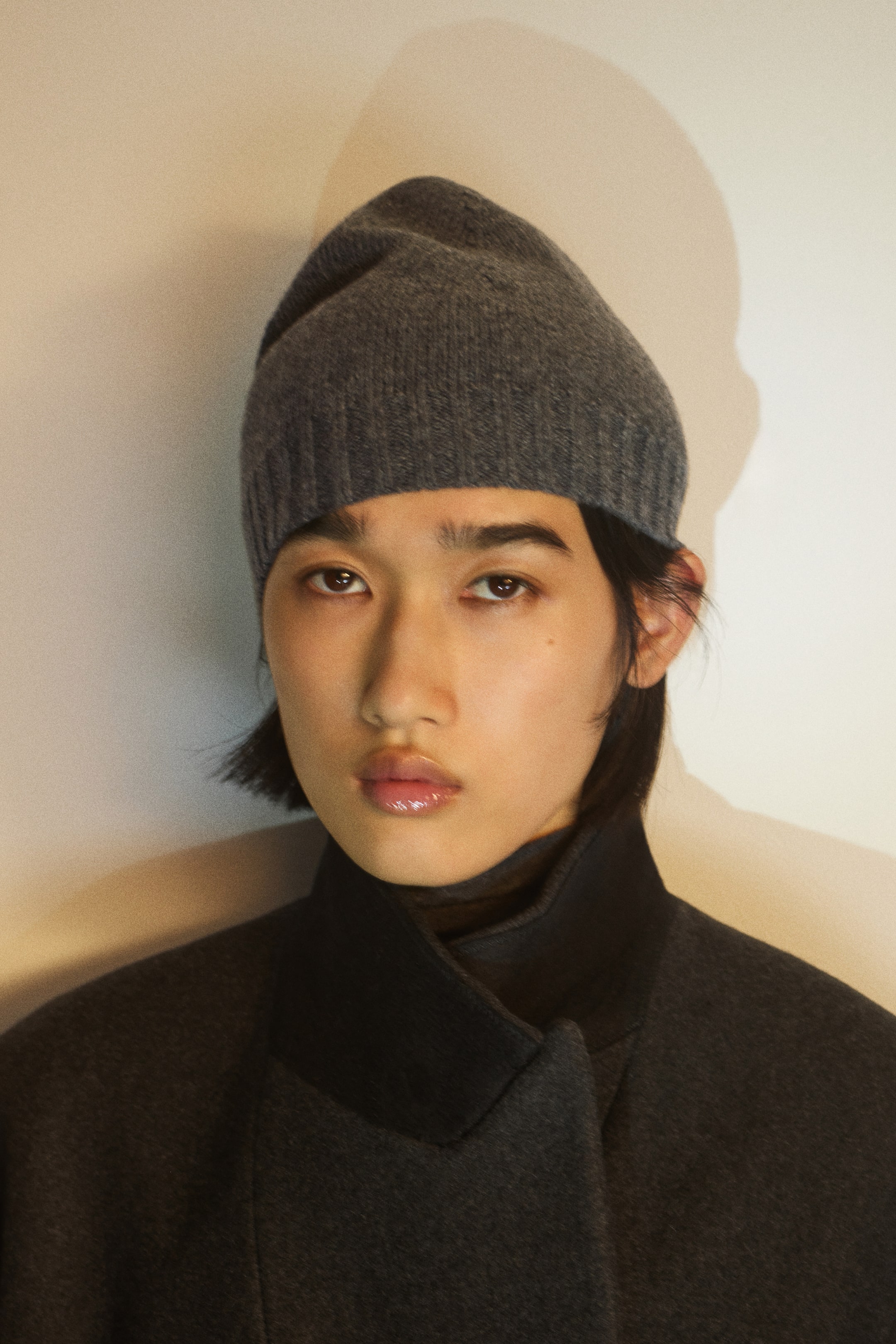 Voir une image plus grande: Un bonnet gris en tricot doux avec un bord côtelé est porté par le mannequin, qui porte également un manteau gris foncé avec un col montant structuré.