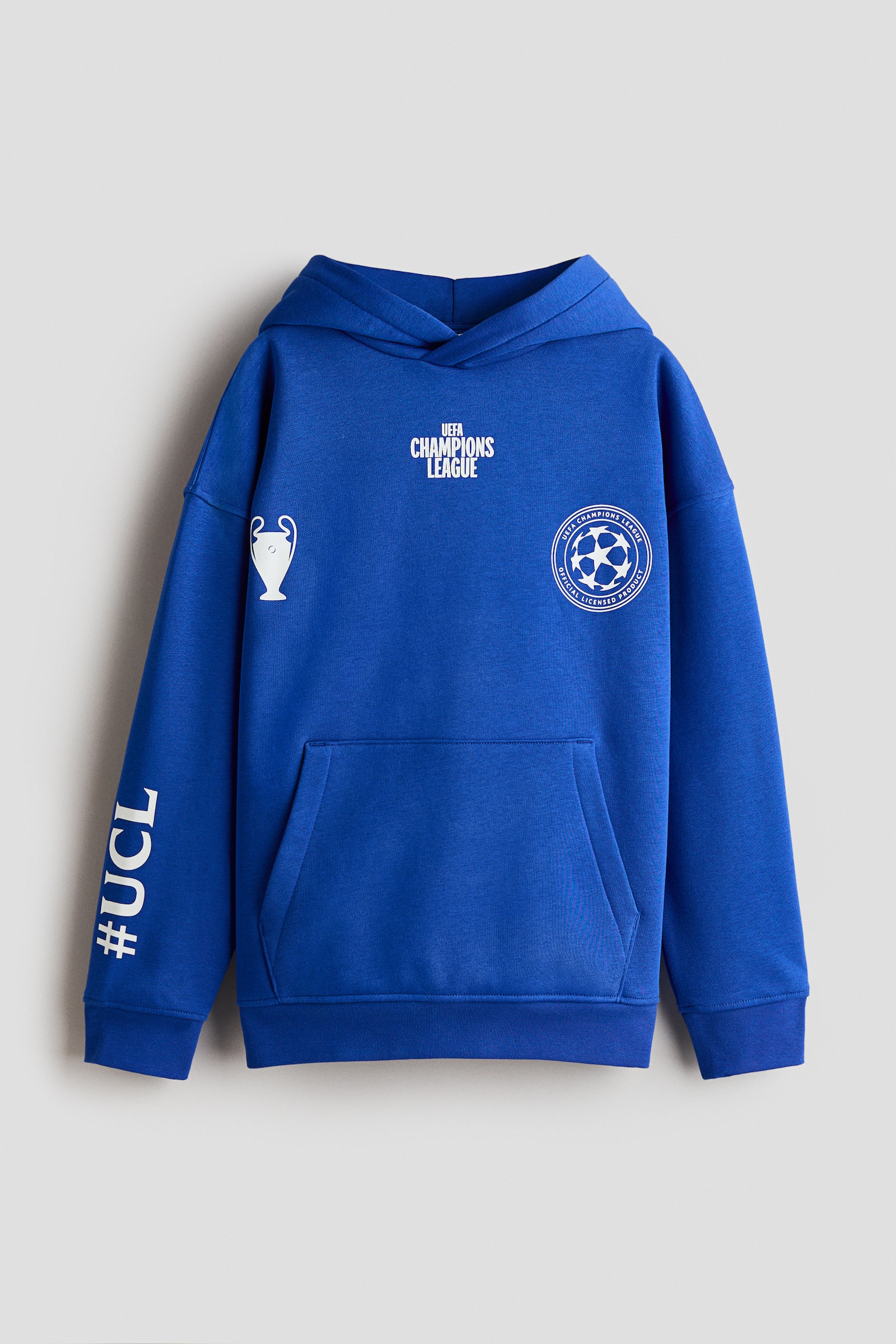 Un hanorac din material fleece albastru este prezentat din faÈÄ Èi are glugÄ tip wrap-front, umeri cÄzuÈi, buzunar kangaroo Èi finisaje ribate la manÈete Èi tiv. Hanoracul este detaliat cu grafice imprimate albe, inclusiv textul âUEFA CHAMPIONS LEAGUEâ, o pictogramÄ de trofeu, un logo circular Èi â#UCLâ imprimat vertical pe mânecÄ.