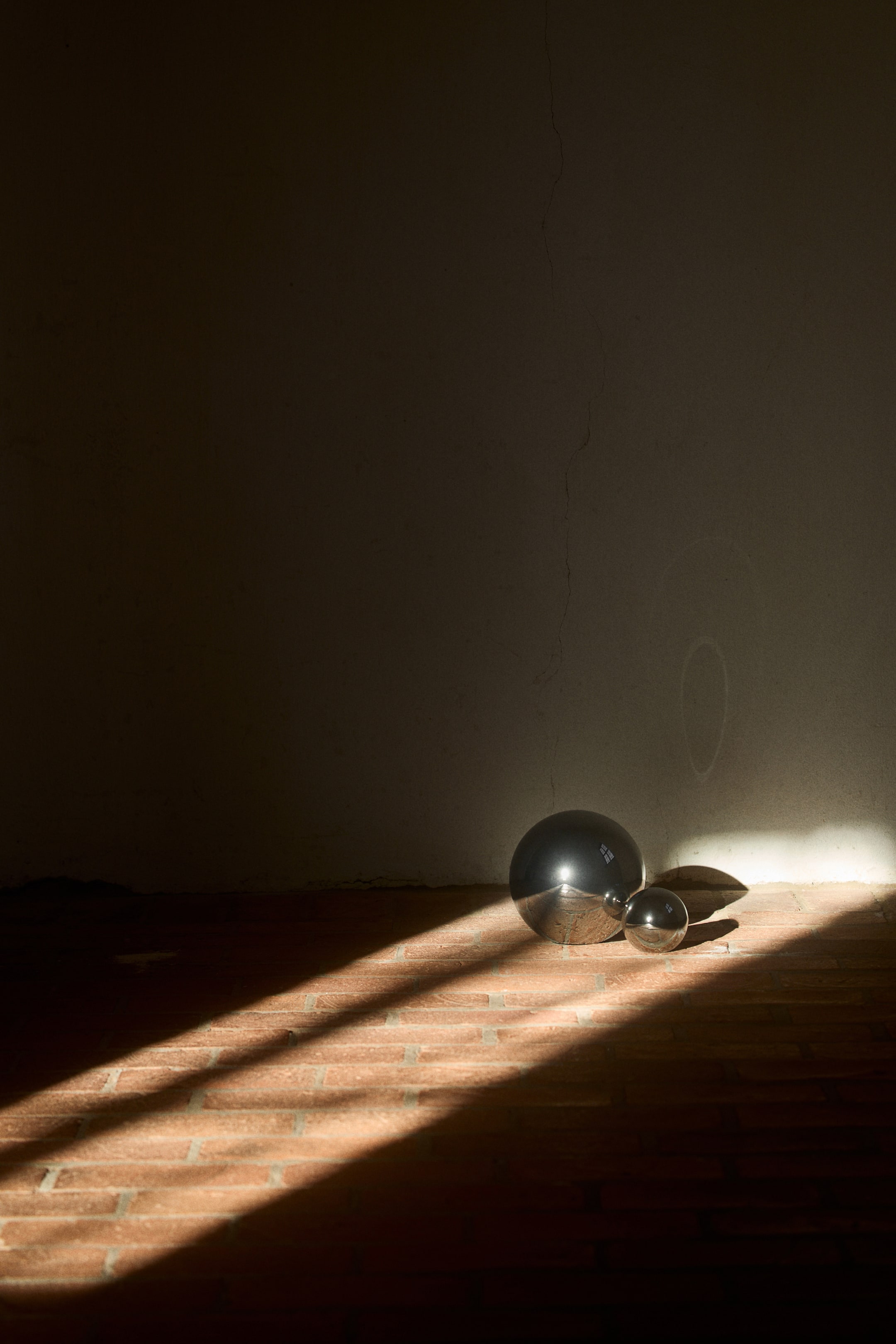View larger image: A larger polished metallic sphere is positioned behind a smaller polished metallic sphere. Both are reflecting bright light.