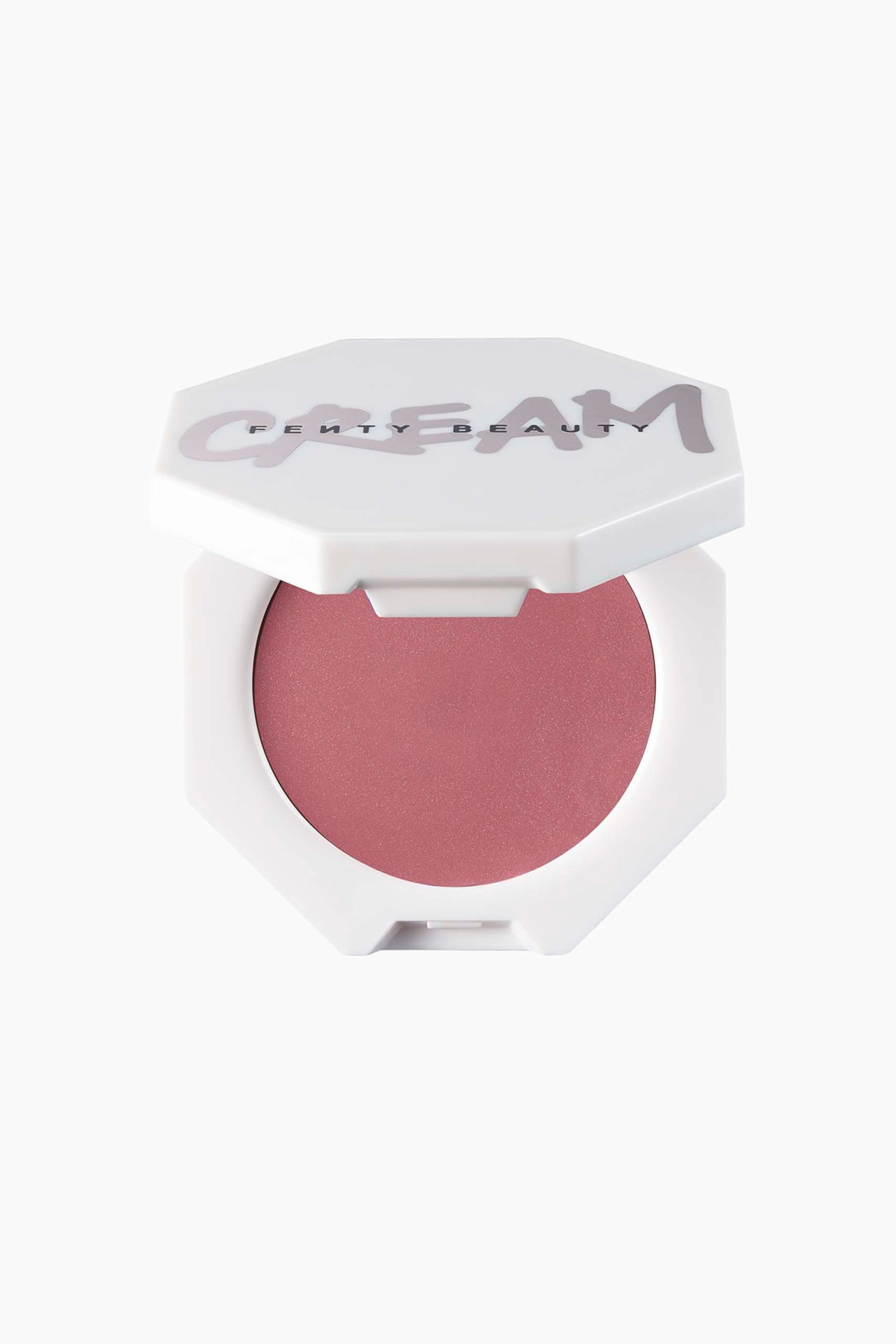Näytä suurempi kuva: Cheeks Out Freestyle Cream Blush lepää avoimessa valkoisessa kahdeksankulmaisessa kompaktissa eteenpäin suunnattuna, ja siinä näkyy pyöreä annos pölyisen ruusun sävyistä voidemaista poskipunaa. Osittain koholla oleva kansi esittelee sanan "CREAM" tyylitellyllä violetilla käsikirjoitusfontilla, ja sen alla on painettuna "FENTY BEAUTY".