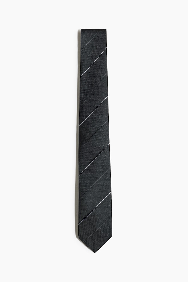 Una corbata negra muestra un patrón de rayas diagonales en su superficie frontal. El patrón presenta líneas punteadas blancas delgadas alternando con rayas sólidas más anchas de color gris oscuro. - 1