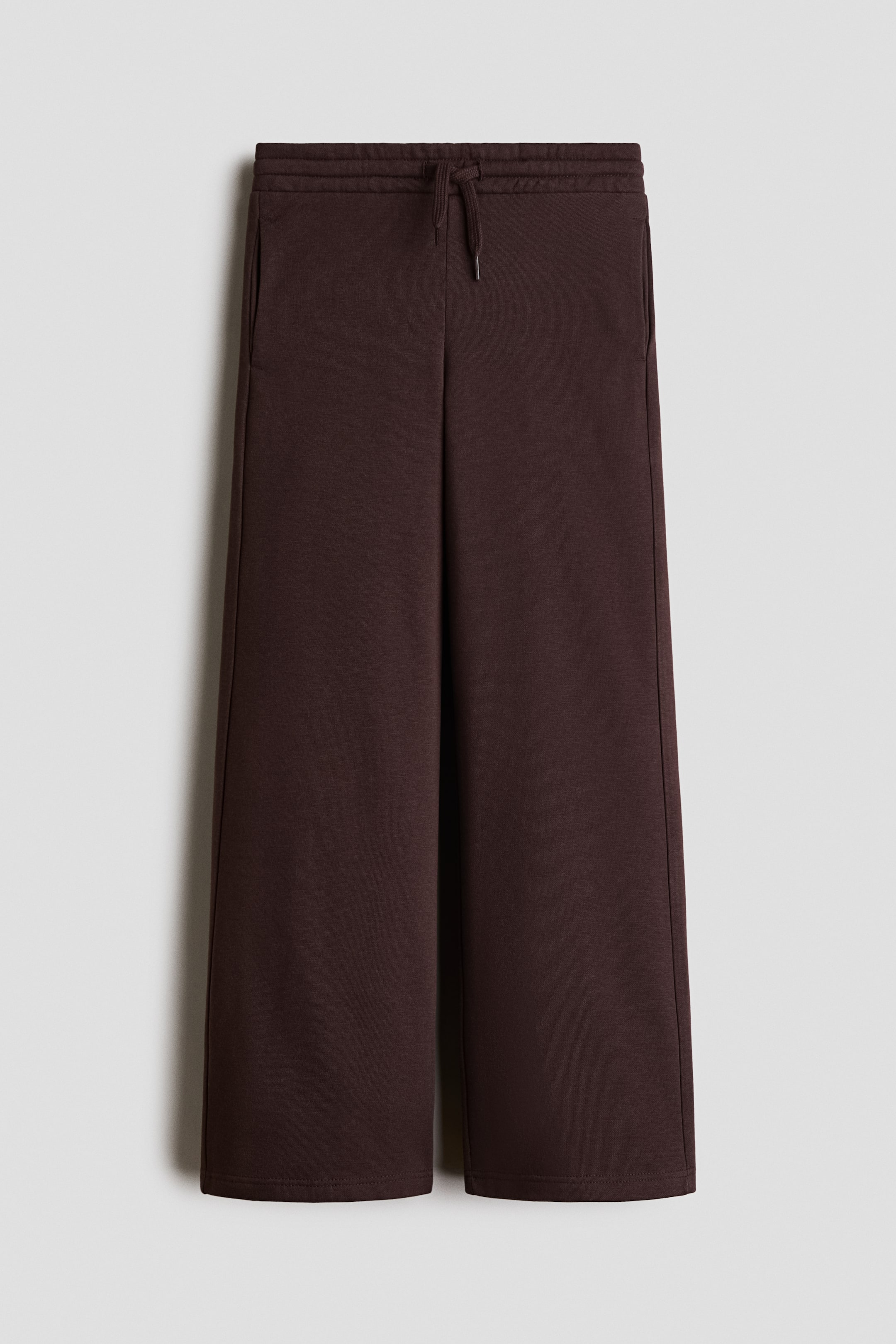 View larger image: The dark brown joggers, made from a visible sweatshirt fabric, are shown from the front, featuring an elasticated drawstring waist with a visible tie, discreet side pockets, and straight legs.
