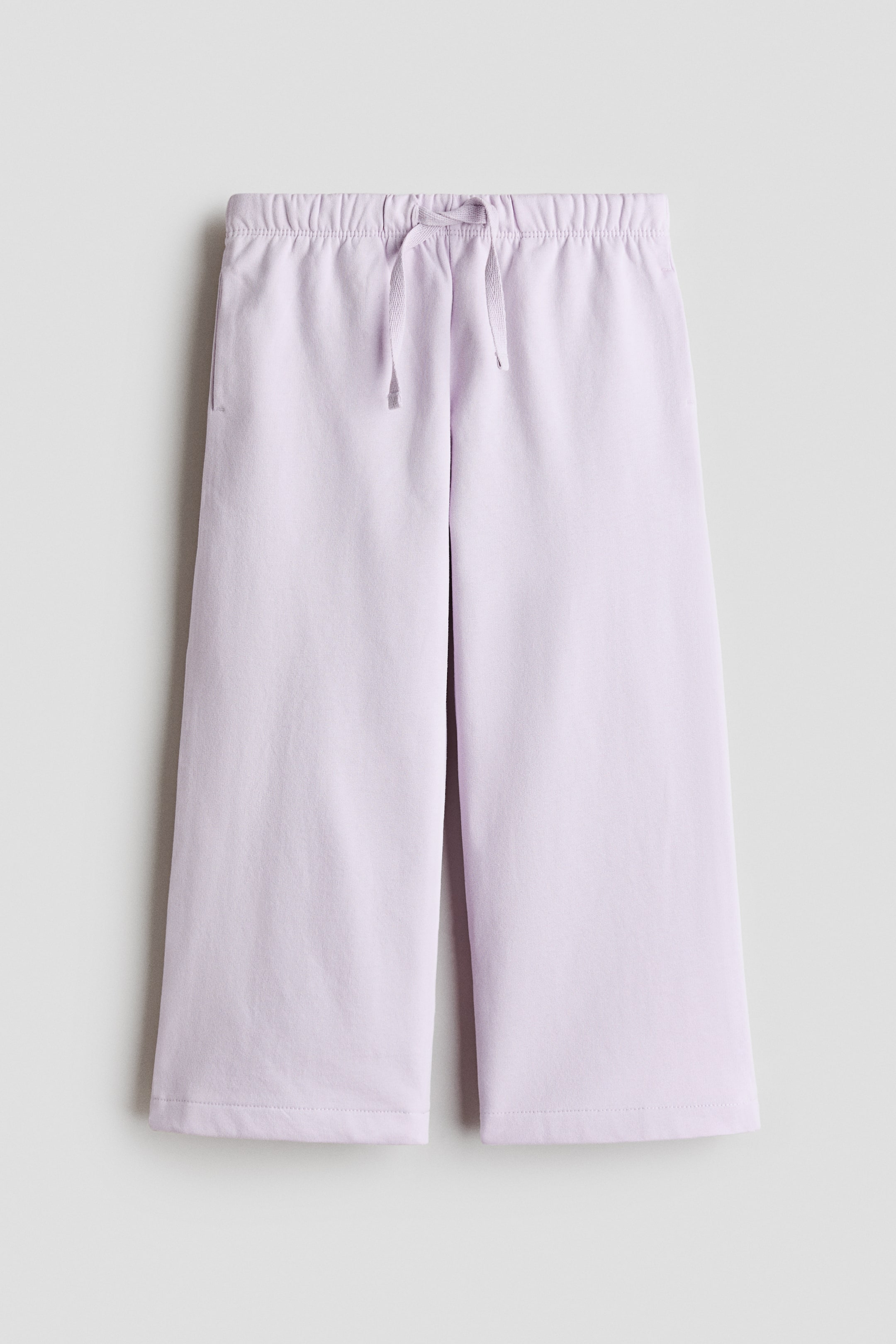 View larger image: Light purple cropped trousers come with an elasticated drawstring waistband, elegantly tied with a bow at the front. On the left side, you'll find a vertical slit pocket, adding to the practicality. These trousers exhibit a relaxed, wide-leg fit, finished with a straight hem, perfect for a chic yet comfortable look.