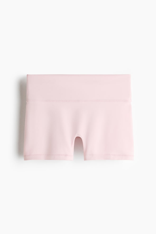Des hotpants de sport en rose clair sont présentés de face. Ils sont dotés d'un tissu lisse, d'une large ceinture taille haute avec des coutures doubles et des jambes courtes avec des ourlets finis proprement et une couture gousset en forme de U visible à l'entrejambe. - 1
