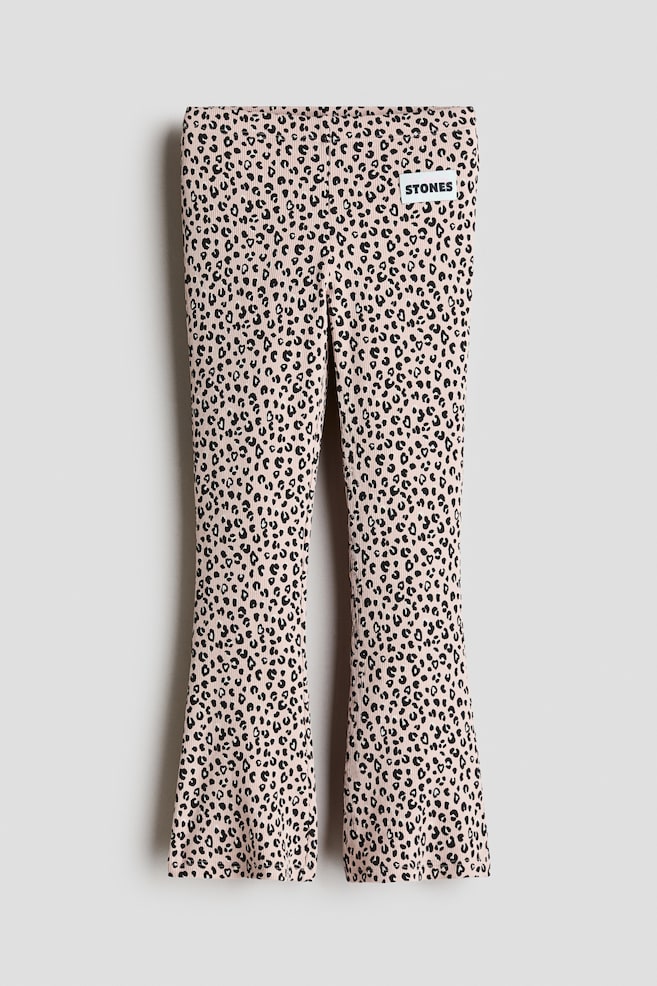 Pantalon Ã©vasÃ© cÃ´telÃ© rose clair, vu de face, avec un imprimÃ© lÃ©opard noir sur lâensemble et une silhouette ajustÃ©e qui sâÃ©largit vers lâourlet. Le pantalon prÃ©sente une taille plate ainsi quâun petit patch rectangulaire blanc de la marque sur le haut de la cuisse gauche. - 1