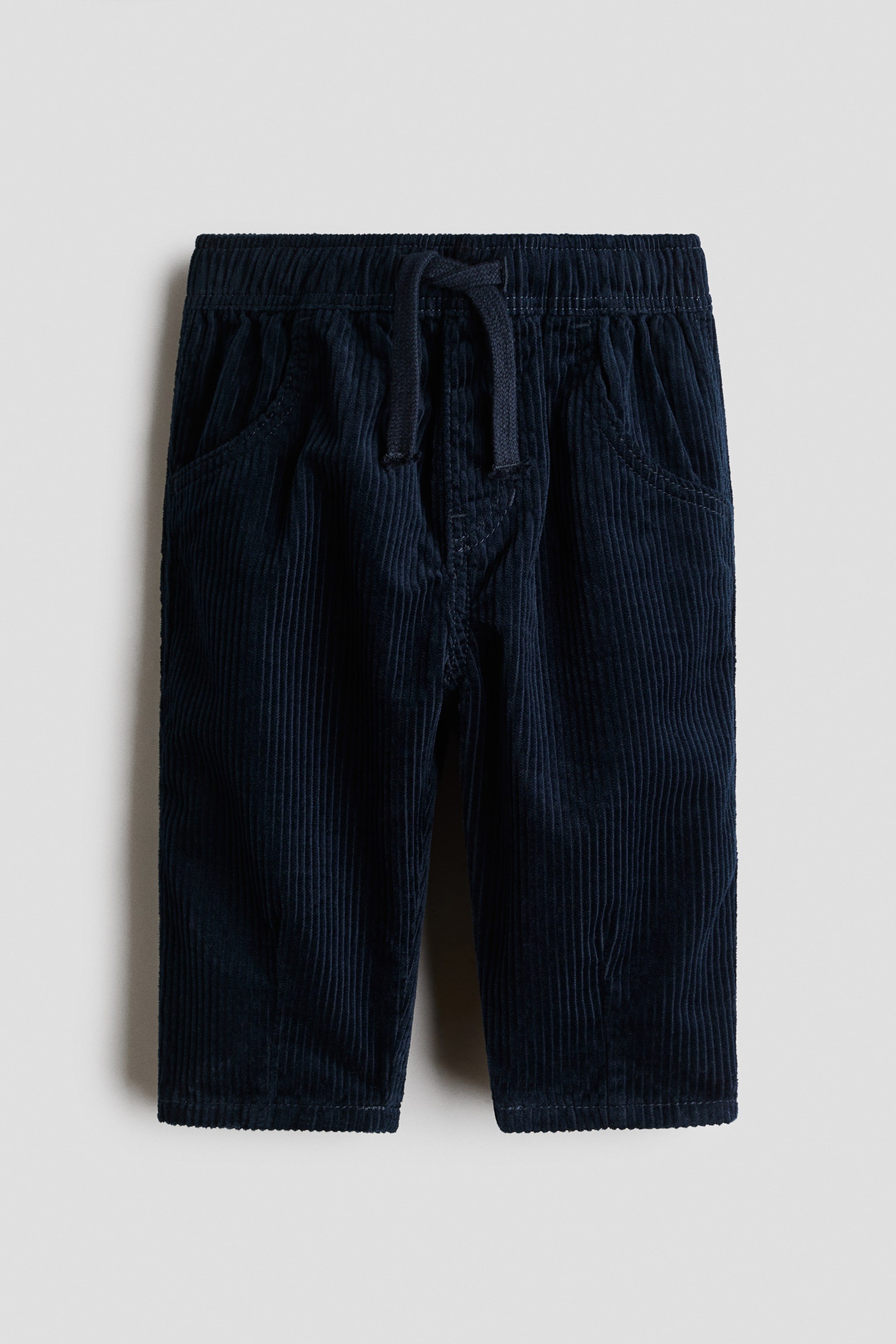Agrandir l'image: Pantalon en velours côtelé bleu foncé présenté de face, doté d'une taille élastiquée avec un cordon de serrage visible. Le pantalon est également muni de deux poches avant passepoilées et d'un ourlet simple.