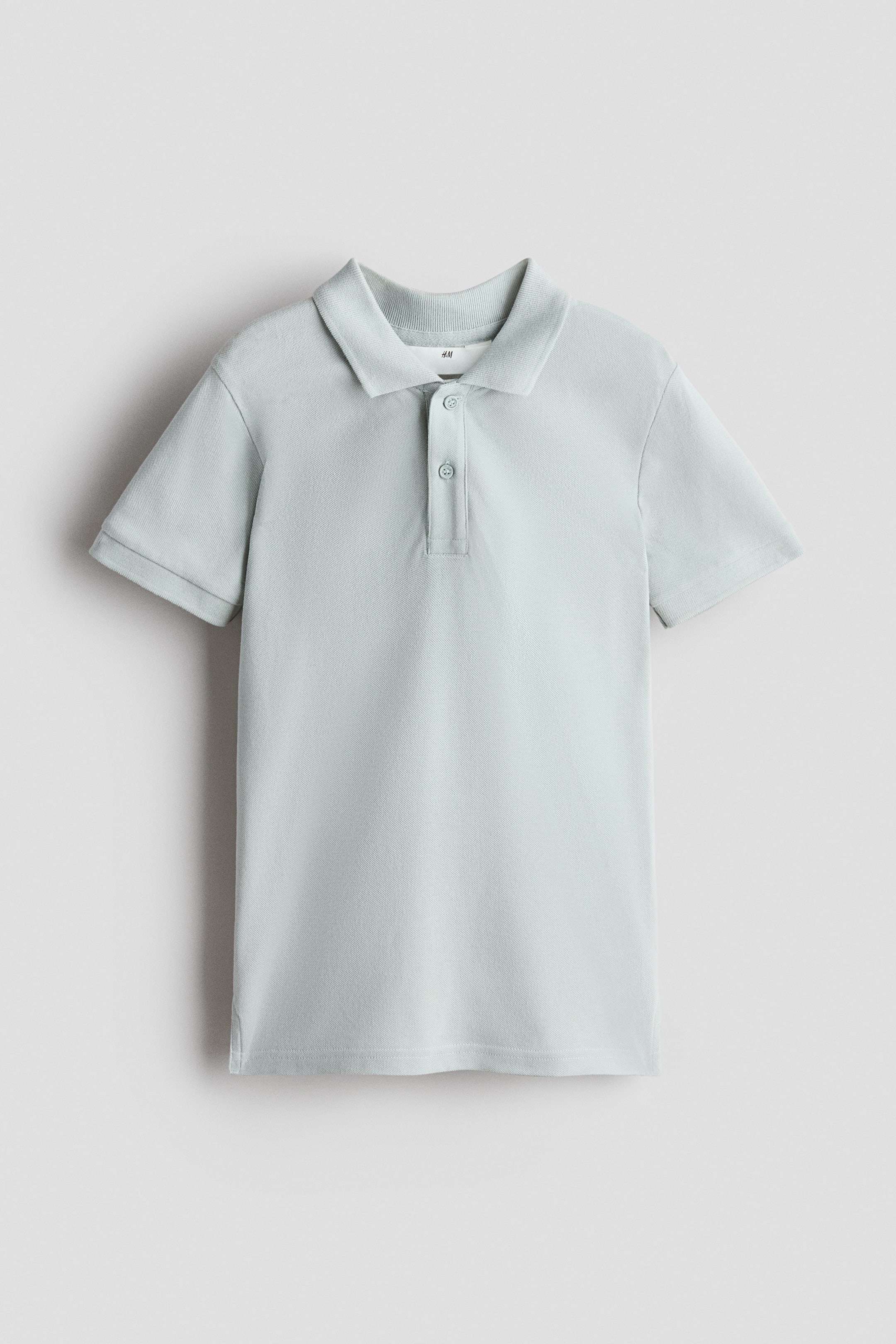 Voir une image plus grande: Un polo en maille piquée d'un vert bleu pâle est suspendu, de face, doté d'un col côtelé, d'une patte de boutonnage à deux boutons assortis et de manches courtes.