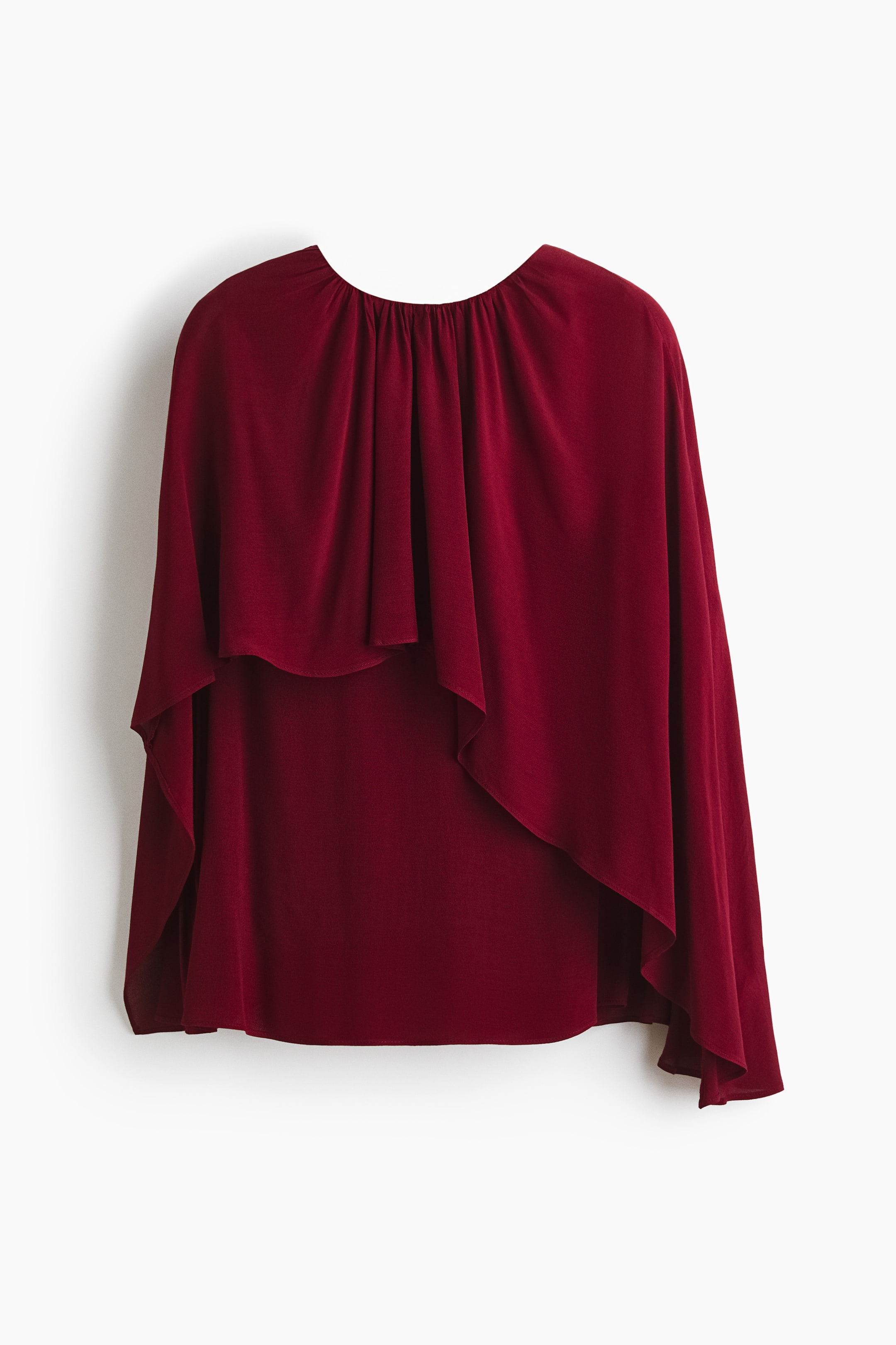 View larger image: A rich maroon blouse showcases its front, boasting a gathered round neckline. A flowing cape-like overlay elegantly drapes over the main body, with the overlay featuring an asymmetrical hemline above the straight hem of the lower body.