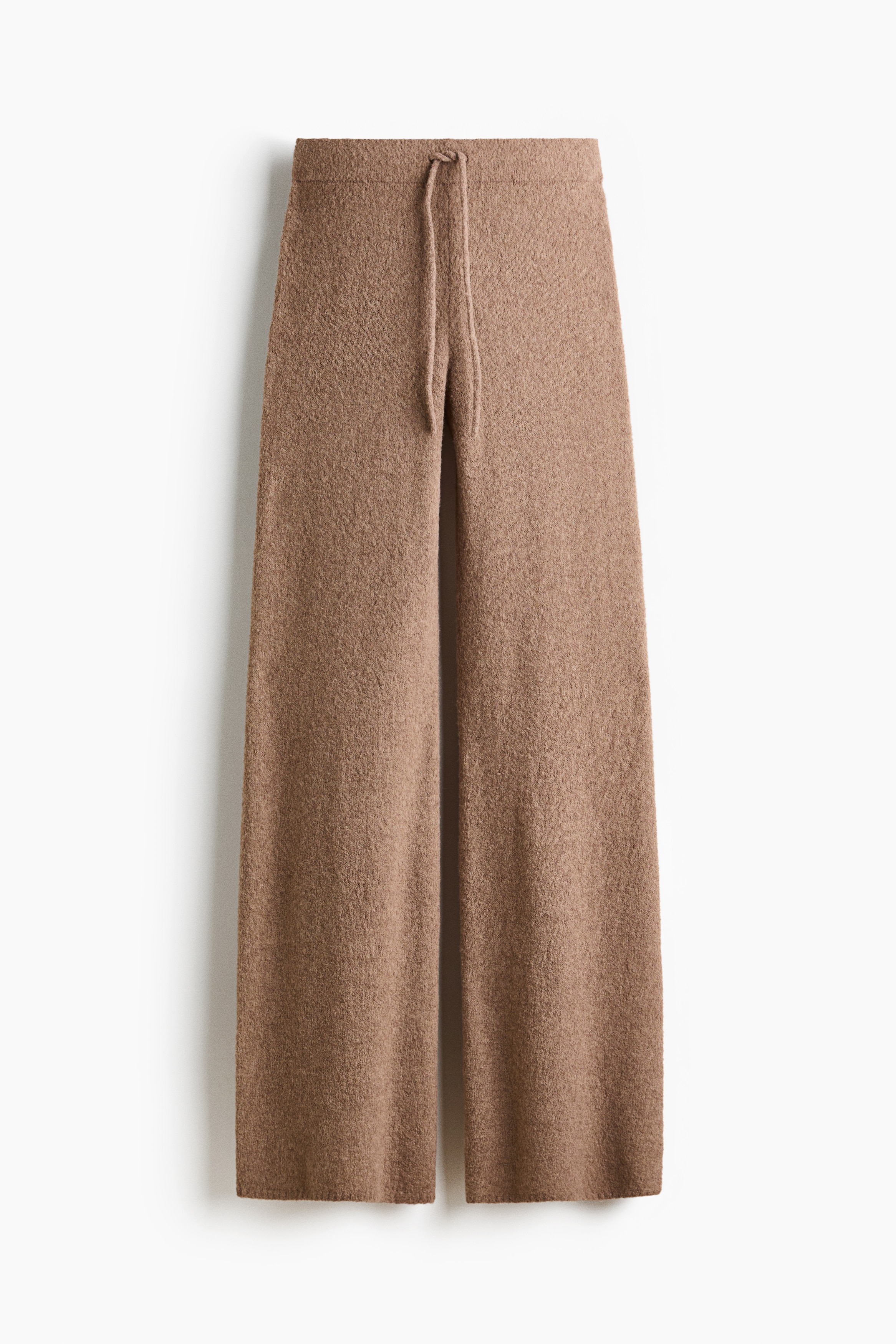 A brown, textured knit mock-neck jumper with ribbed cuffs is being worn by the model, paired with matching knit trousers. The model is crouching, showcasing the relaxed drape and soft material of the coordinating set.