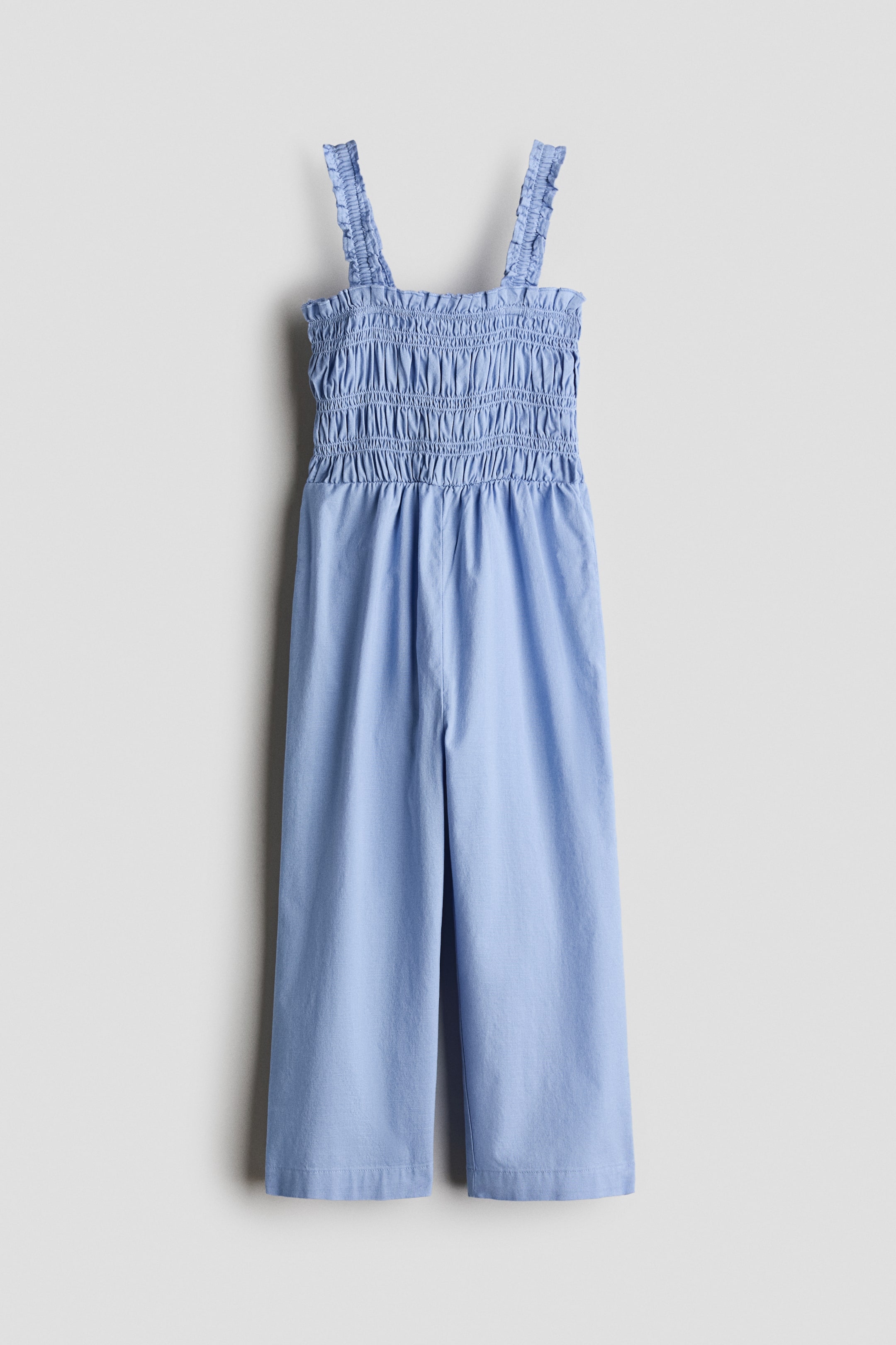 View larger image: A light blue jumpsuit showcases its FRONT, highlighting a shirred bodice and waist, ruffled shoulder straps, and wide-leg pants.