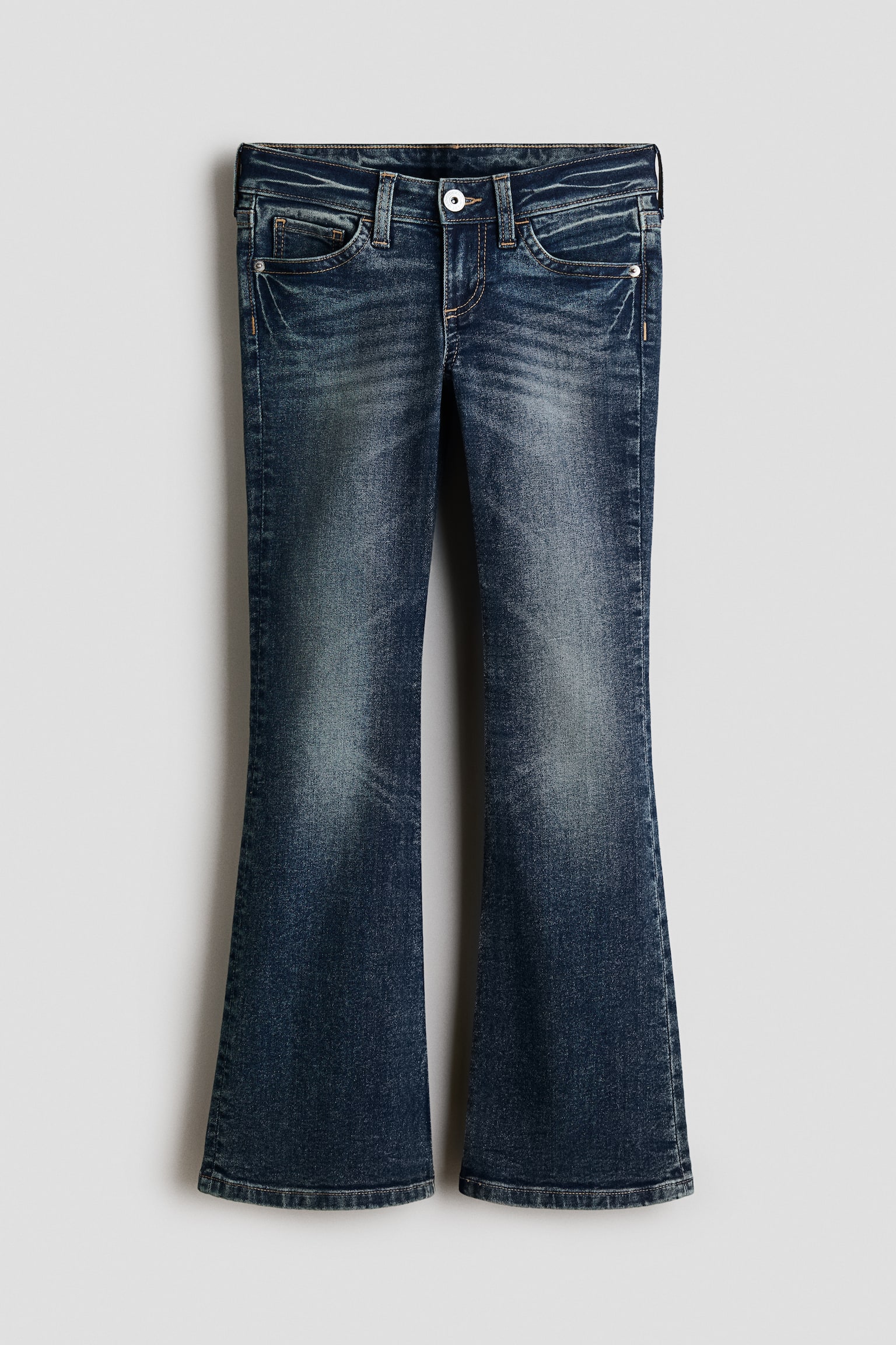 Ein Paar dunkel gewaschene blaue Denim-Jeans ist in der Vorderansicht zu sehen und zeigt ein Five-Pocket-Design mit Low-Rise-Bund und Knopfverschluss. Die Jeans haben eine Slim-Fit-Passform an HÃ¼fte und Oberschenkeln, die zu ausgestellten BeinabschlÃ¼ssen hin weiter wird, mit leichten Ausbleichungen auf der Vorderseite der Beine.