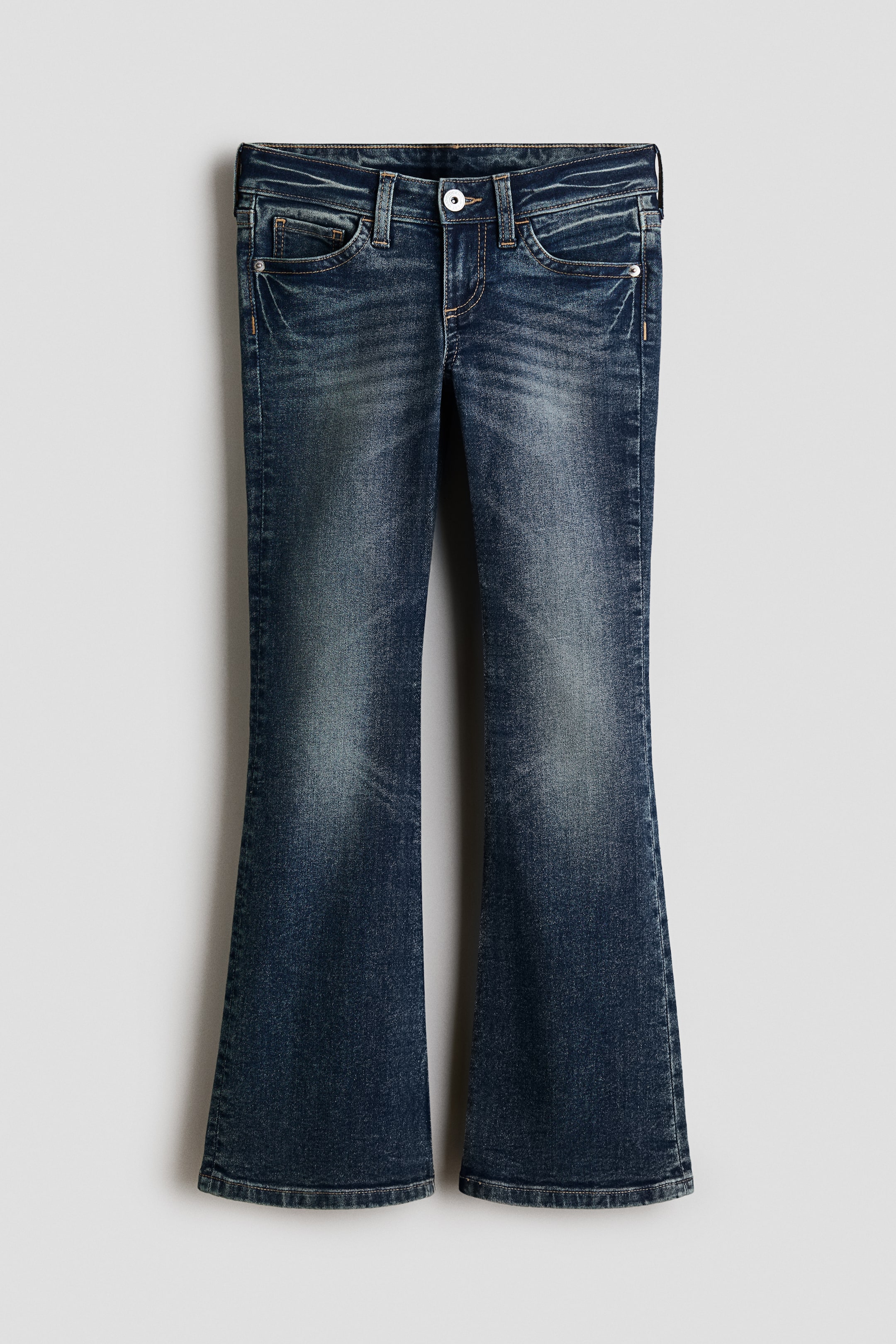 Visa större bild: Ett par mörkblå jeans i denim visas framifrån och uppvisar en femficksdesign med låg midja och knäppning med knapp. Jeansen har en slim fit över höfter och lår som övergår i utsvängda benslut, med lätt blekning på framsidan av benen.
