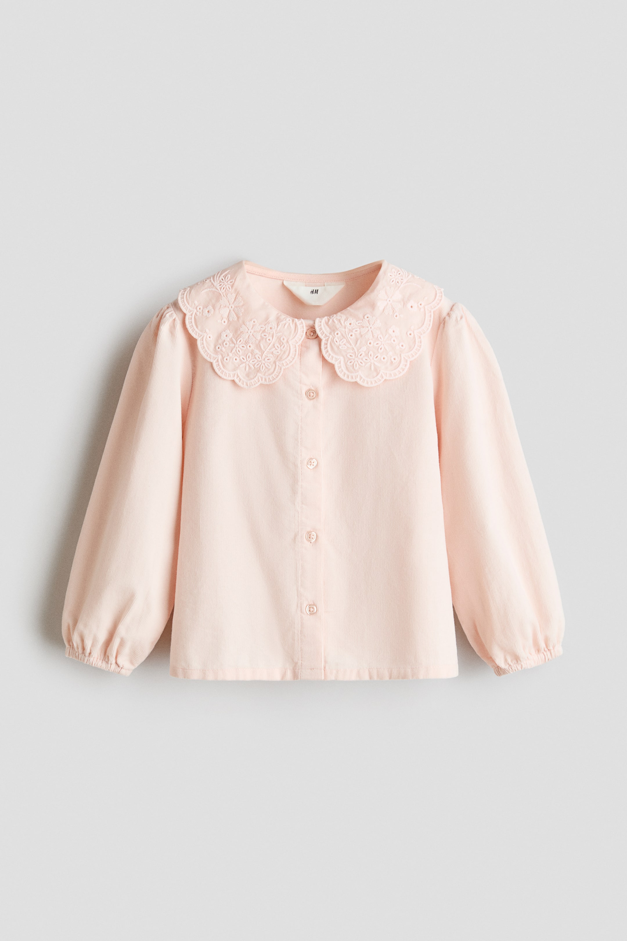 View larger image: A light pink long-sleeved shirt is shown from the front, featuring a fine ribbed texture and a large scalloped collar with tone-on-tone eyelet embroidery. It has puffed shoulders, elasticated cuffs, and a full button placket with matching buttons running down the front.