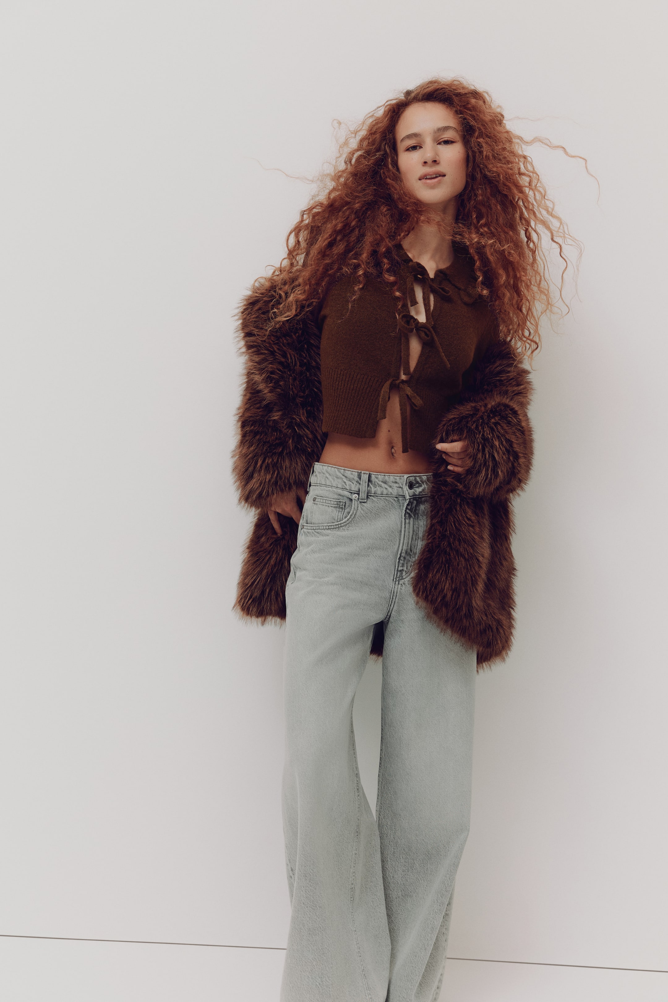 拡大画像を表示: ブラウンのフェイクファーコートが羽織るようにオープンに掛けられ、シャギーな質感とふんわりとしたボリュームのある長めの袖が際立っています。