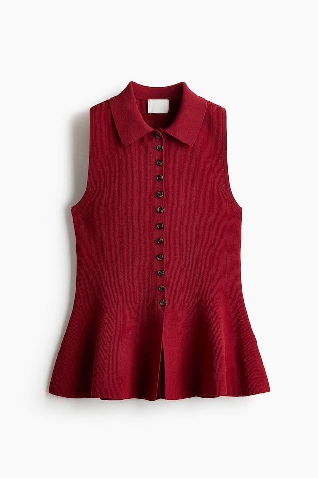 A deep red sleeveless ribbed knit top is laid flat, facing forward, showcasing a pointed collar, a full-length button placket with small dark buttons, and a flared hem with a front slit. - 1