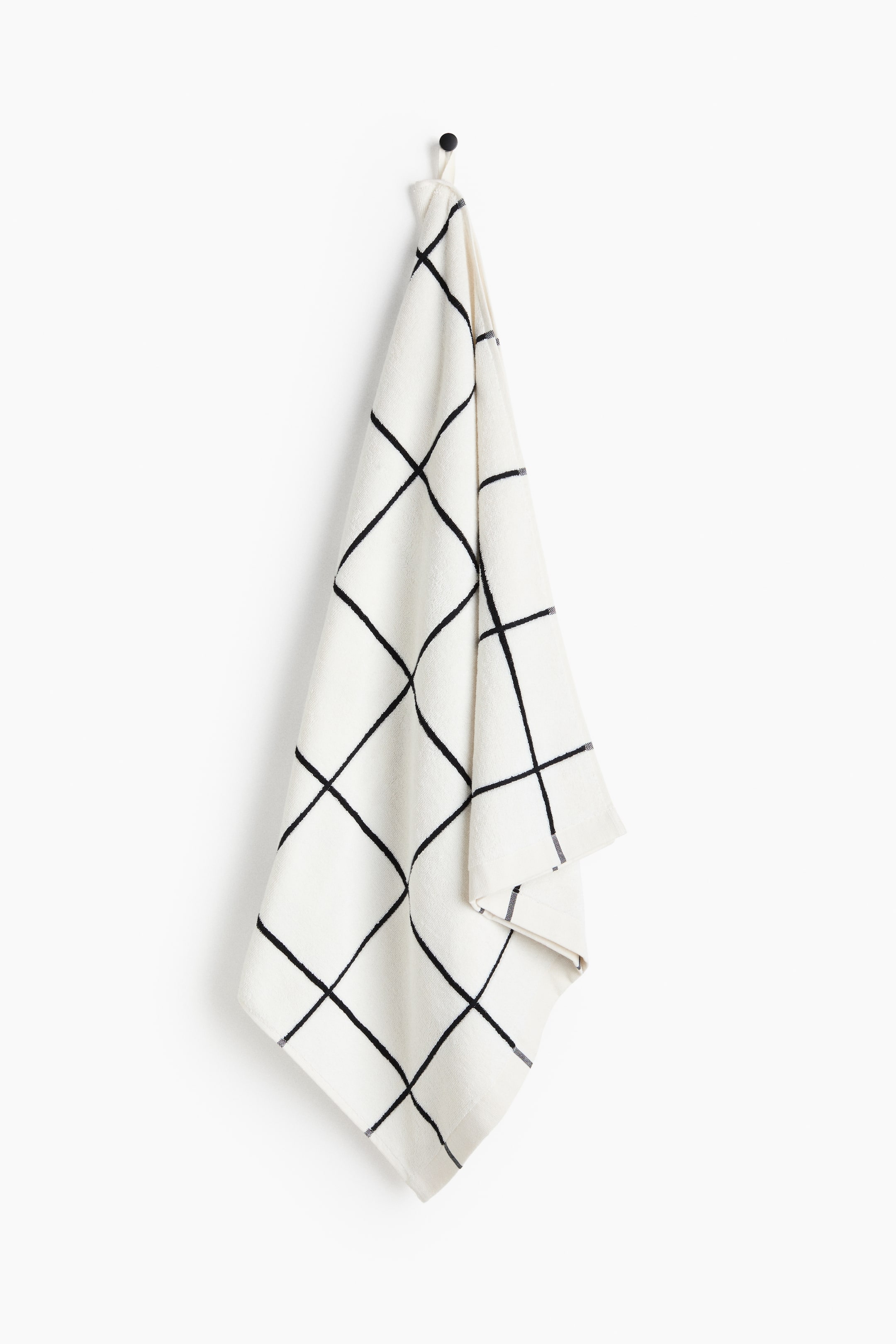 View larger image: A cream-coloured towel featuring an irregular black grid pattern is hanging from a small black hook.