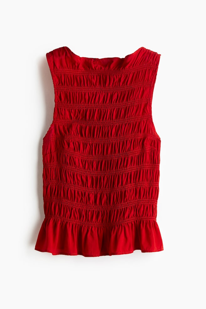 Se presenta un top rojo ajustado y sin mangas de FRENTE, que muestra una silueta completamente fruncida desde su escote de barco con volantes hasta un dobladillo de peplum. - 1