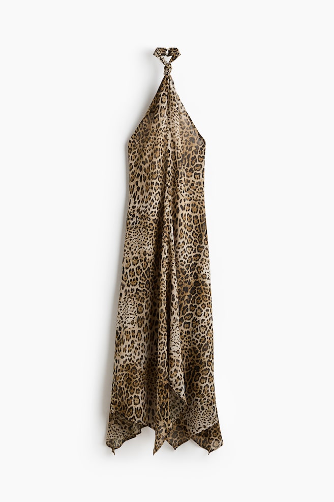 A leopard print halterneck dress is showcasing its front view, featuring a tied neckline and an asymmetrical hem with pointed edges. - 1