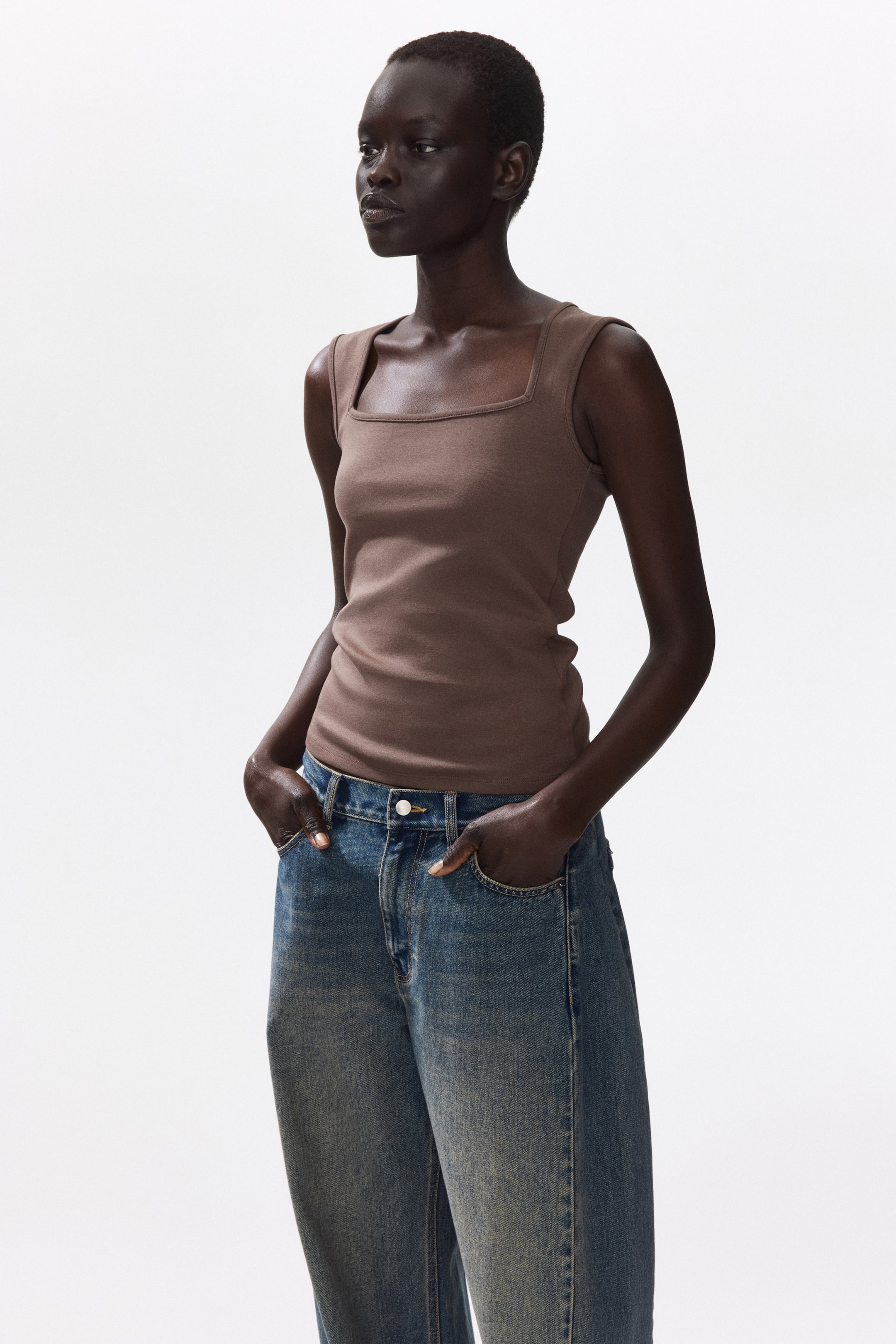 View larger image: A fitted vest top in brown narrow-ribbed cotton jersey, featuring a square neckline and a straight-cut hem, is being worn by the model and tucked into blue jeans.