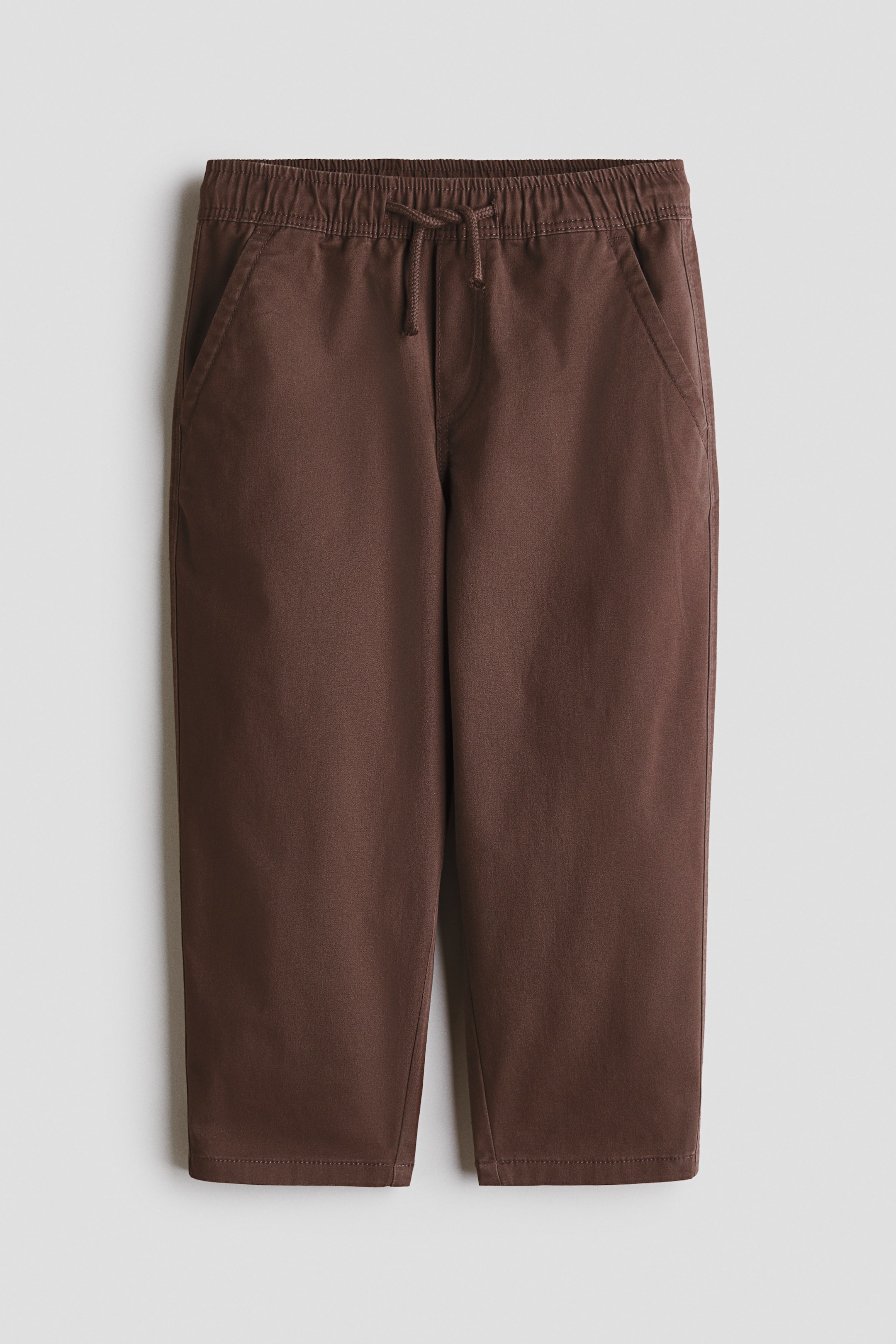View larger image: Brown pants are laid flat, showcasing a front view with an elasticated drawstring waistband, slanted side pockets, straight legs, and a stitched hem.