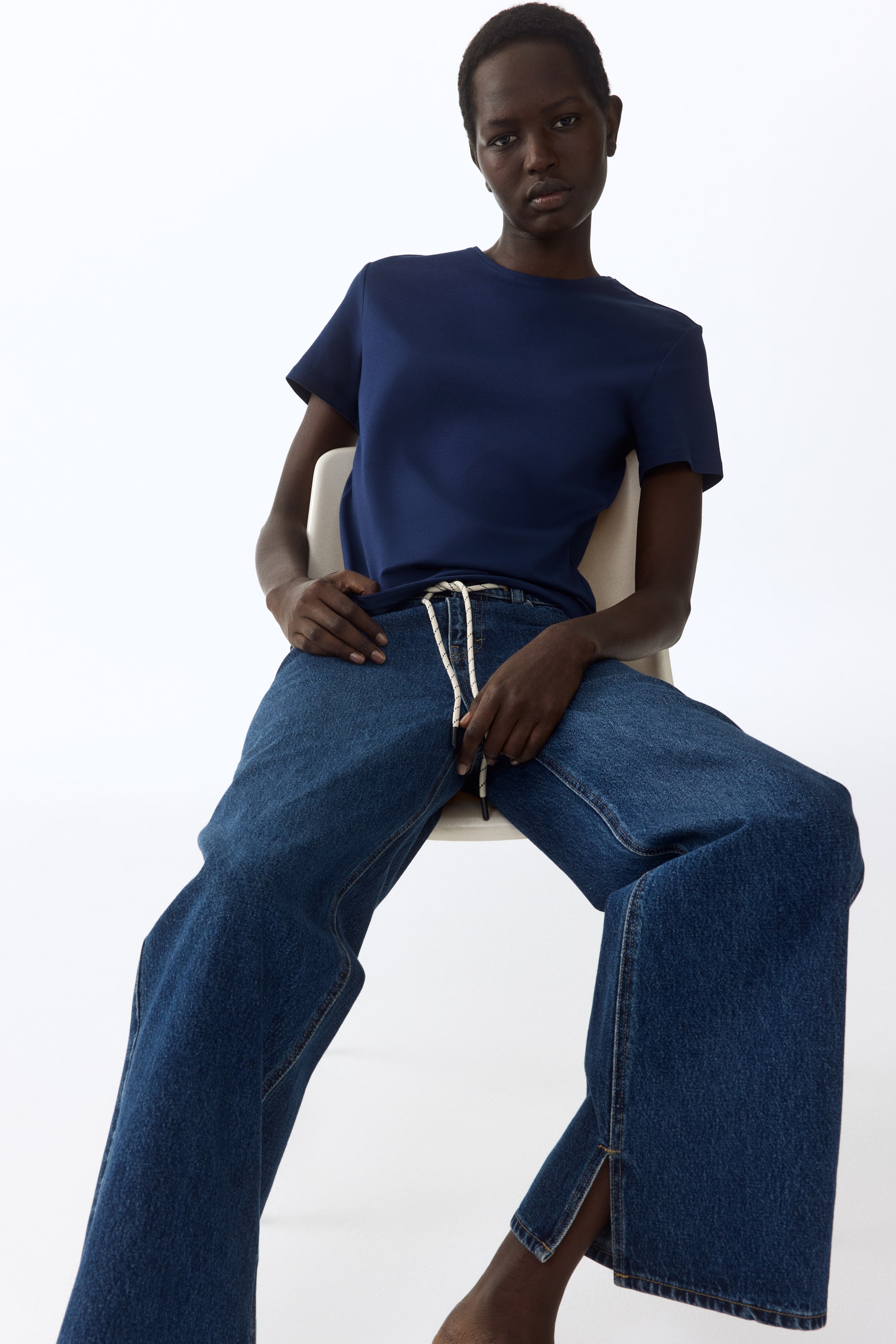 Voir une image plus grande: Jeans en denim bleu avec un cordon de serrage tressé blanc et noir à la taille haute. Le design à jambes larges présente des ourlets fendus sur les coutures extérieures.