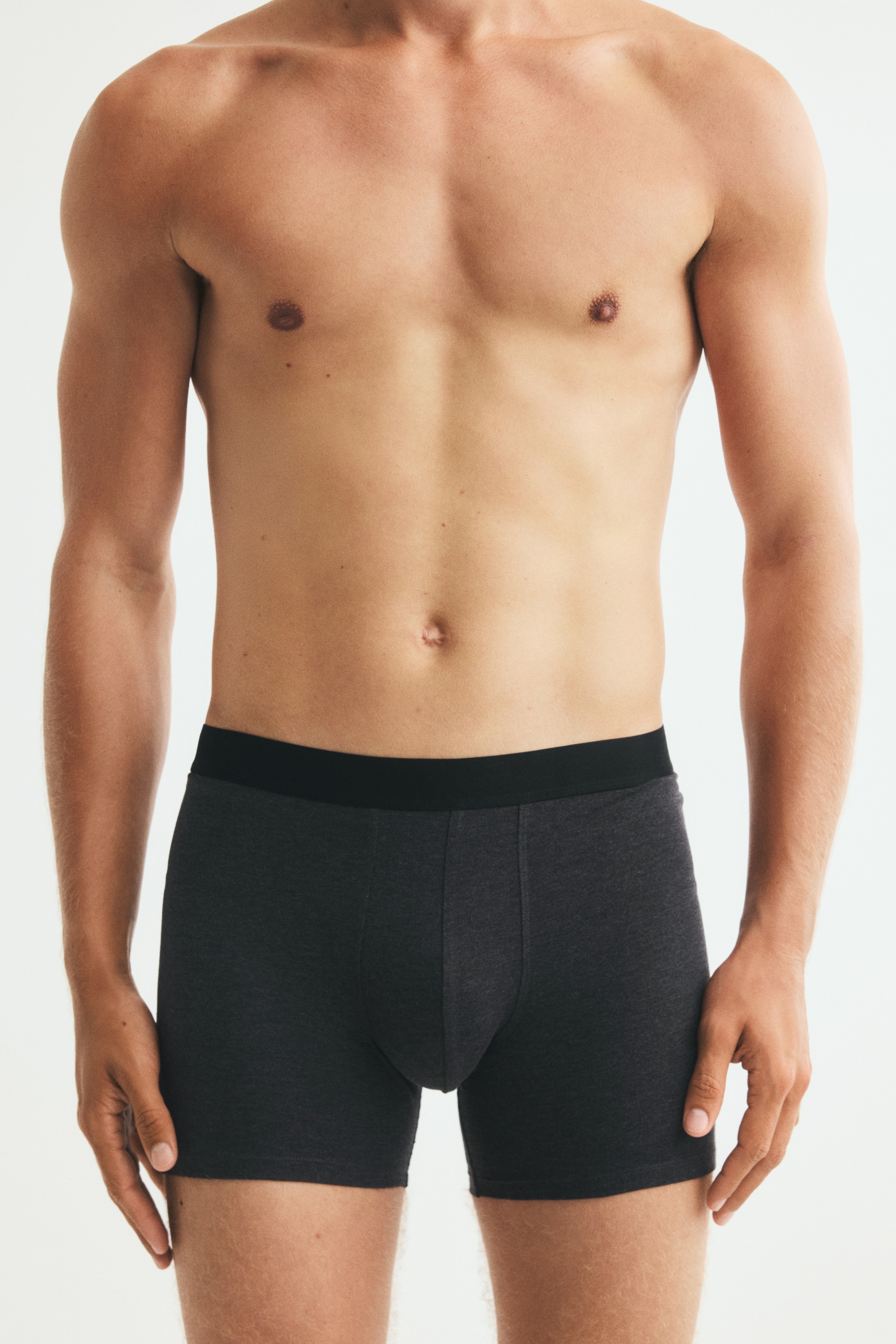 Zwei Stapel Herren-Boxershorts sind ordentlich angeordnet, jeder Stapel enthält mehrere Paare in verschiedenen Schwarz- und Grautönen mit schwarzen elastischen Bündchen.