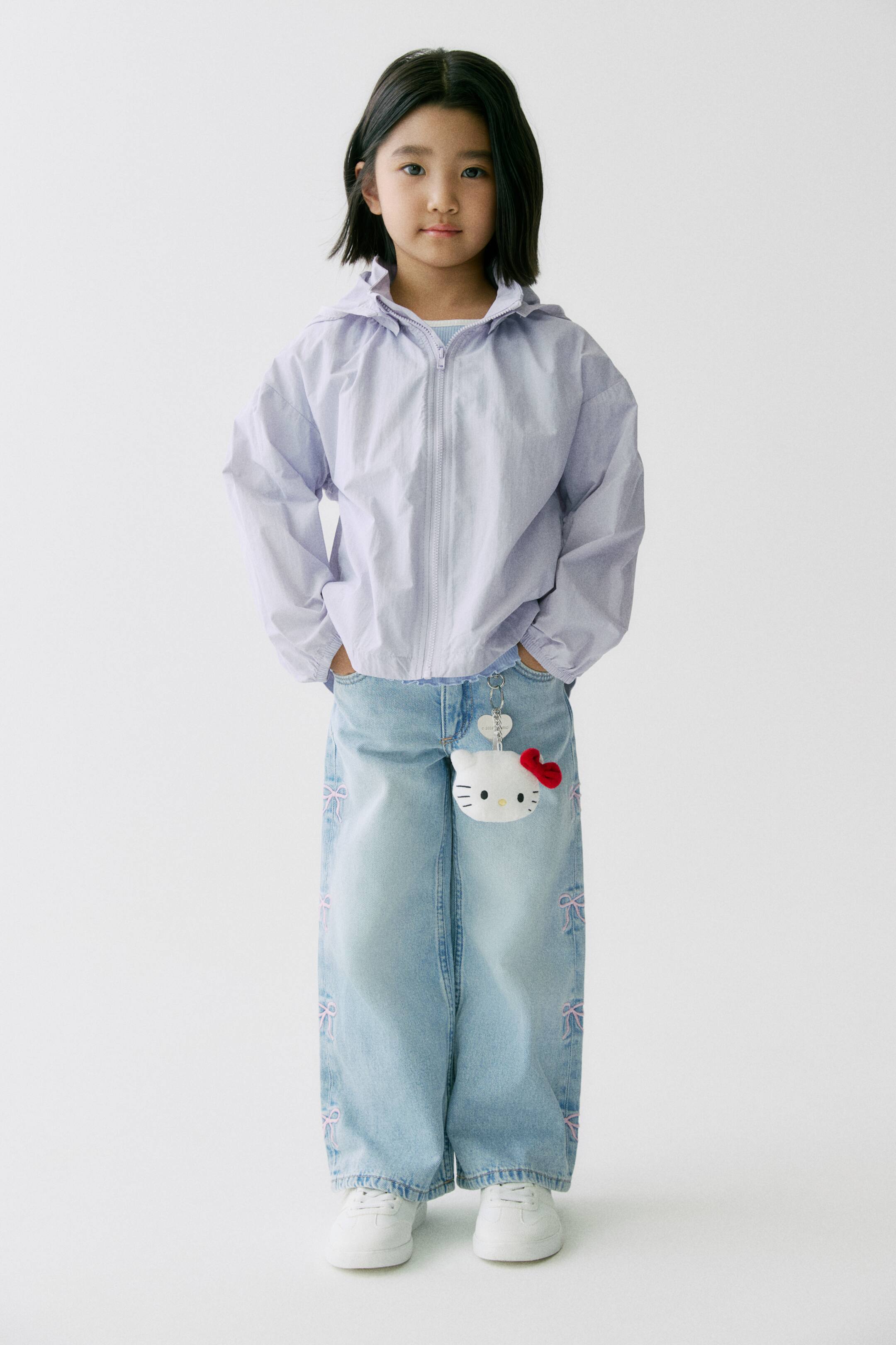 拡大画像を表示: ライトパープルのウインドブレーカーは、フード、スタンドカラー、フロントジップ開閉、ゆったりとしたフィット、ドロップショルダーを備えており、モデルが着用してサイドポケットに手を入れて休ませています。