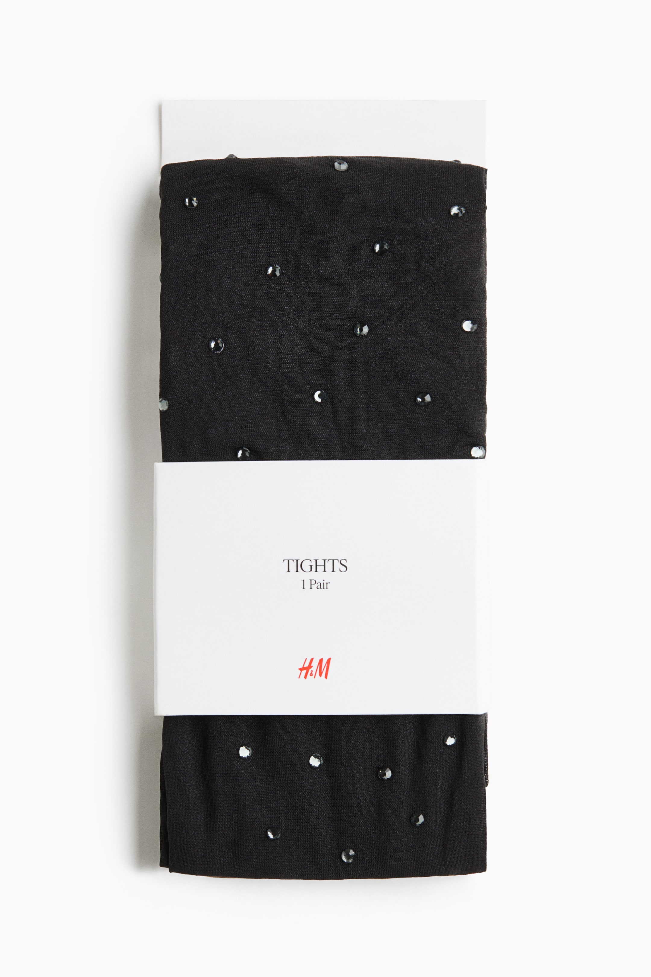 View larger image: A front view of a packaged pair of folded black tights featuring scattered, sparkling rhinestones across the semi-sheer fabric. The tights are wrapped around a white cardboard insert and secured with a white paper band displaying the brand logo and product details.