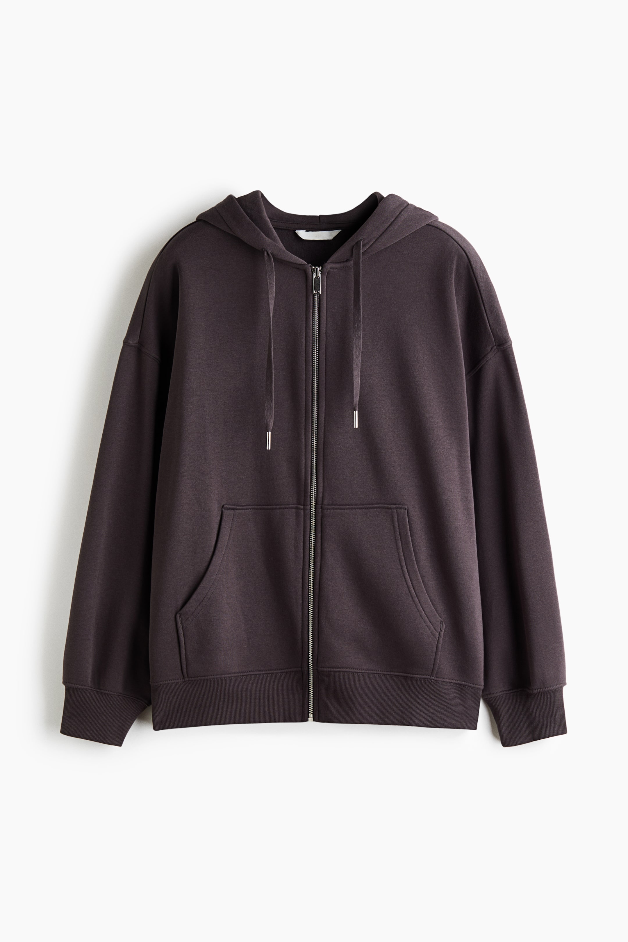Grotere afbeelding bekijken: Een oversized hoodie met ritssluiting in een donkere bruine tint wordt van voren getoond, met een zilverkleurige ritssluiting aan de voorkant, een dubbellaagse capuchon met trekkoorden en verlaagde schouders. Het ontwerp bevat gesplitste kangoeroezakken aan de voorkant, lange mouwen en geribde details bij de manchetten en zoom.