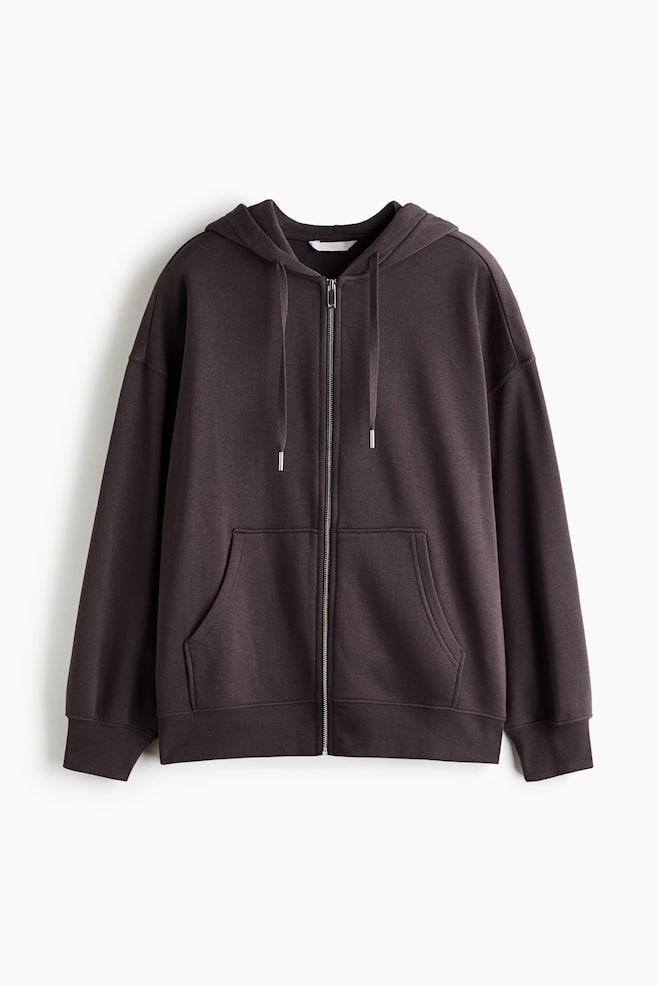 Ein oversized Zip-up-Hoodie in Dunkelbraun ist von vorne zu sehen und verfÃ¼gt Ã¼ber einen silbernen FrontreiÃverschluss, eine doppellagige Kapuze mit Kordelzug sowie tief angesetzte, Ã¼berschnittene Schultern. Das Design umfasst geteilte KÃ¤ngurutaschen auf der Vorderseite, lange Ãrmel und gerippte Details an BÃ¼ndchen und Saum. - 1