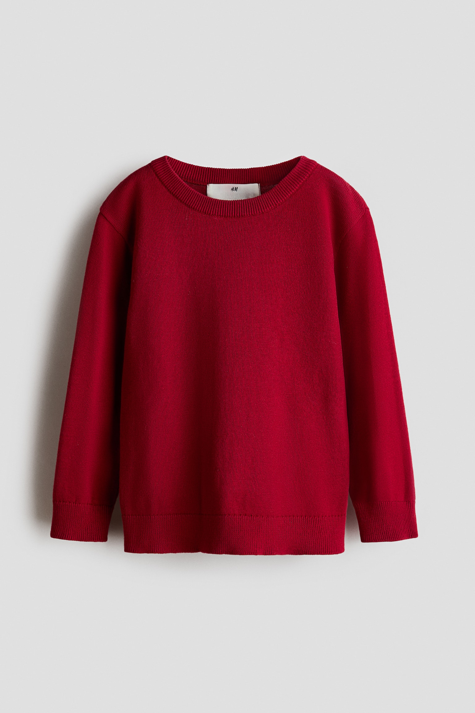 A red fine-knit cotton sweater is shown from the front, featuring a round, rib-trimmed neckline, long sleeves with ribbed cuffs, and a ribbed hem.